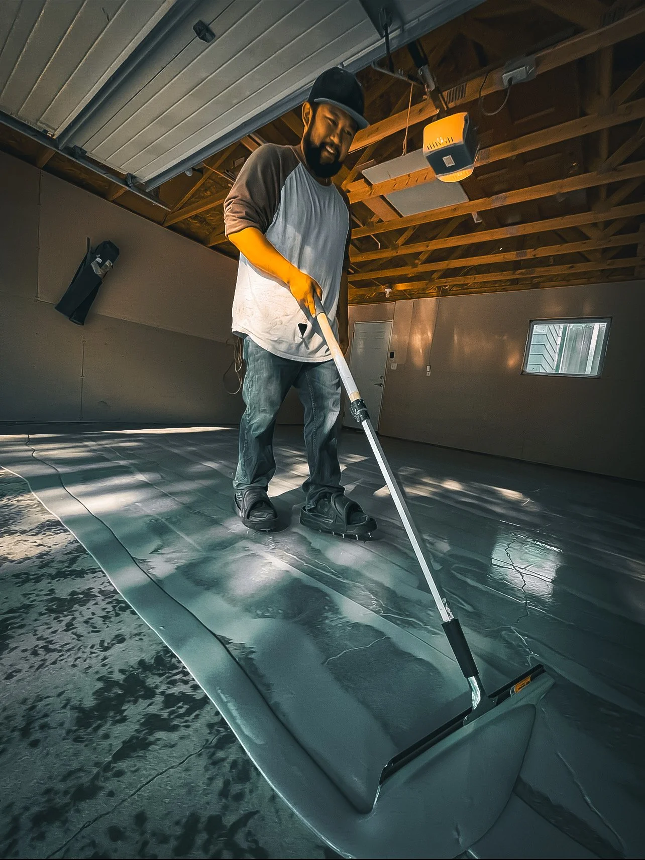 A person applying epoxy floor coating in a garage using a roller. Epoxy services in Winnipeg.