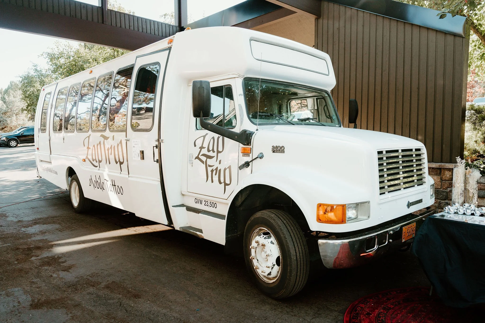White snack truck with 'Zap Trip' logo parked outdoors near a building, with a table covered in items nearby.
