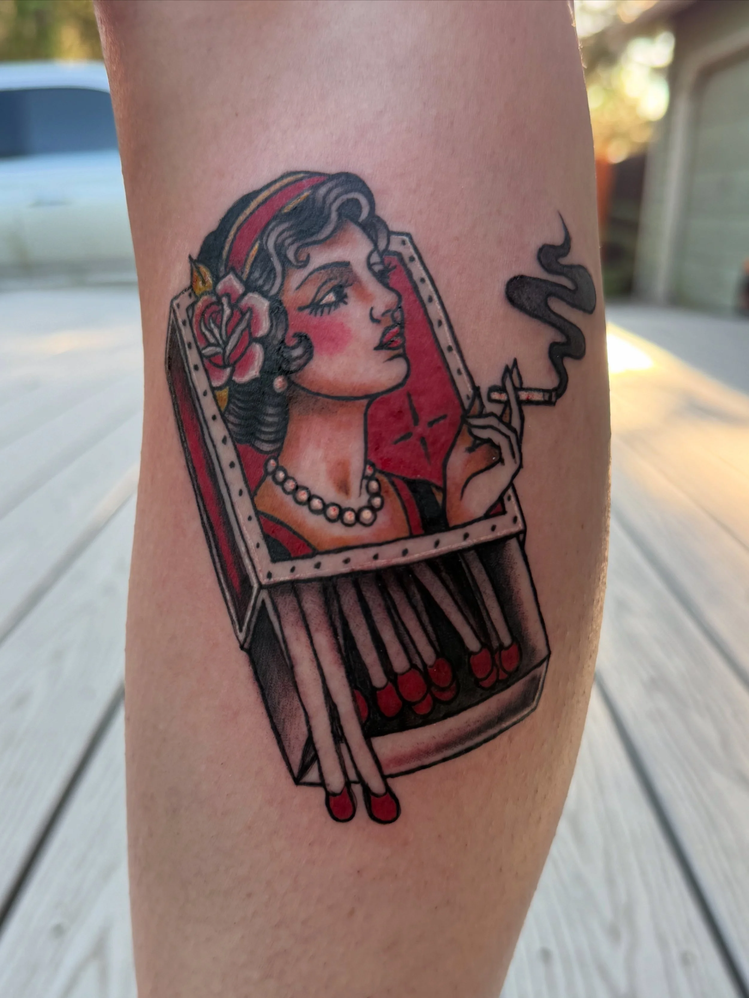 Tattoo of a woman with vintage pin-up style makeup and hair, sitting in an open lipstick case, holding a cigarette, with a pink and red color scheme.