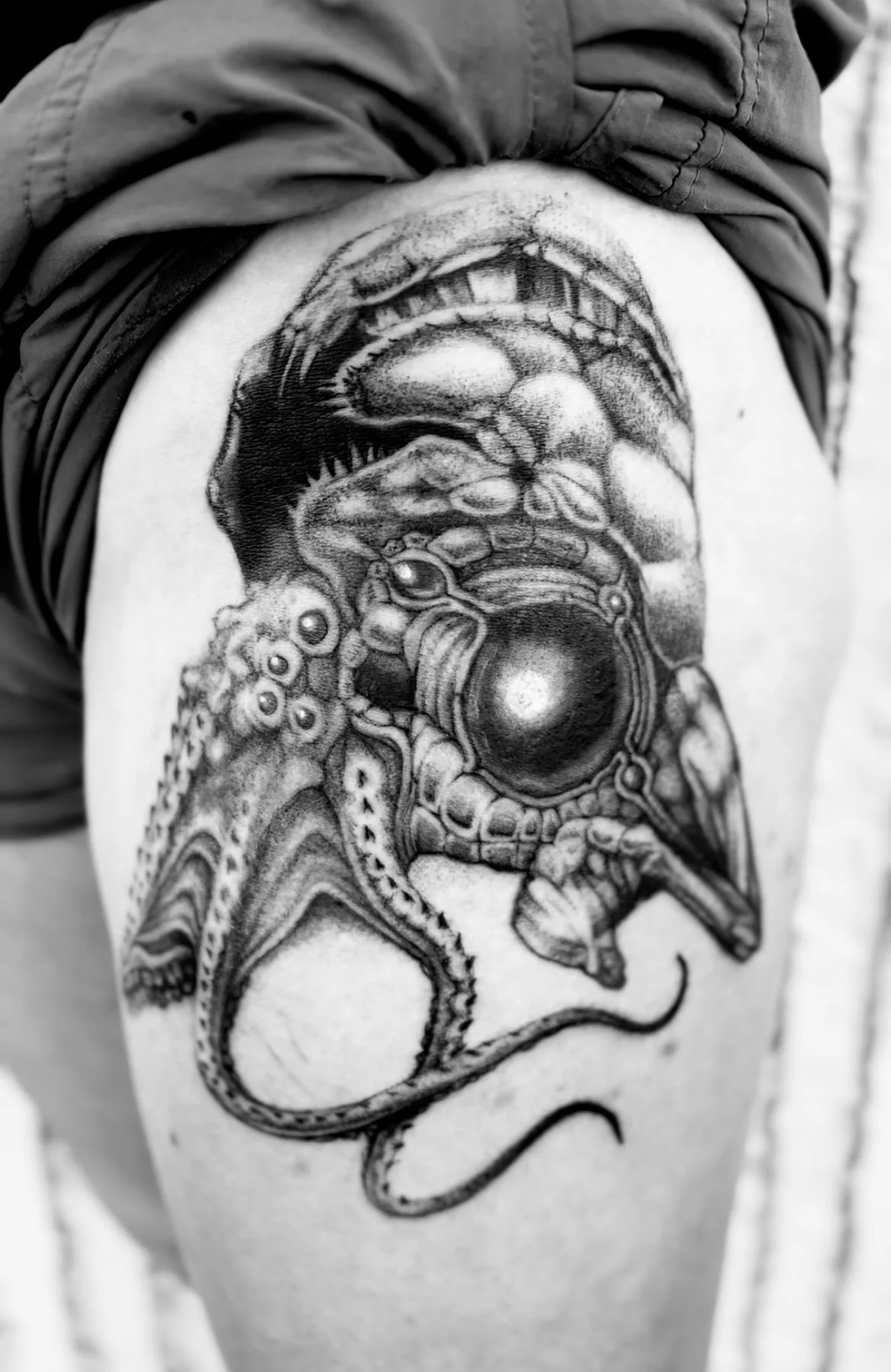 Black and gray tattoo of an octopus and a creature with a large spherical head on a person's upper arm.