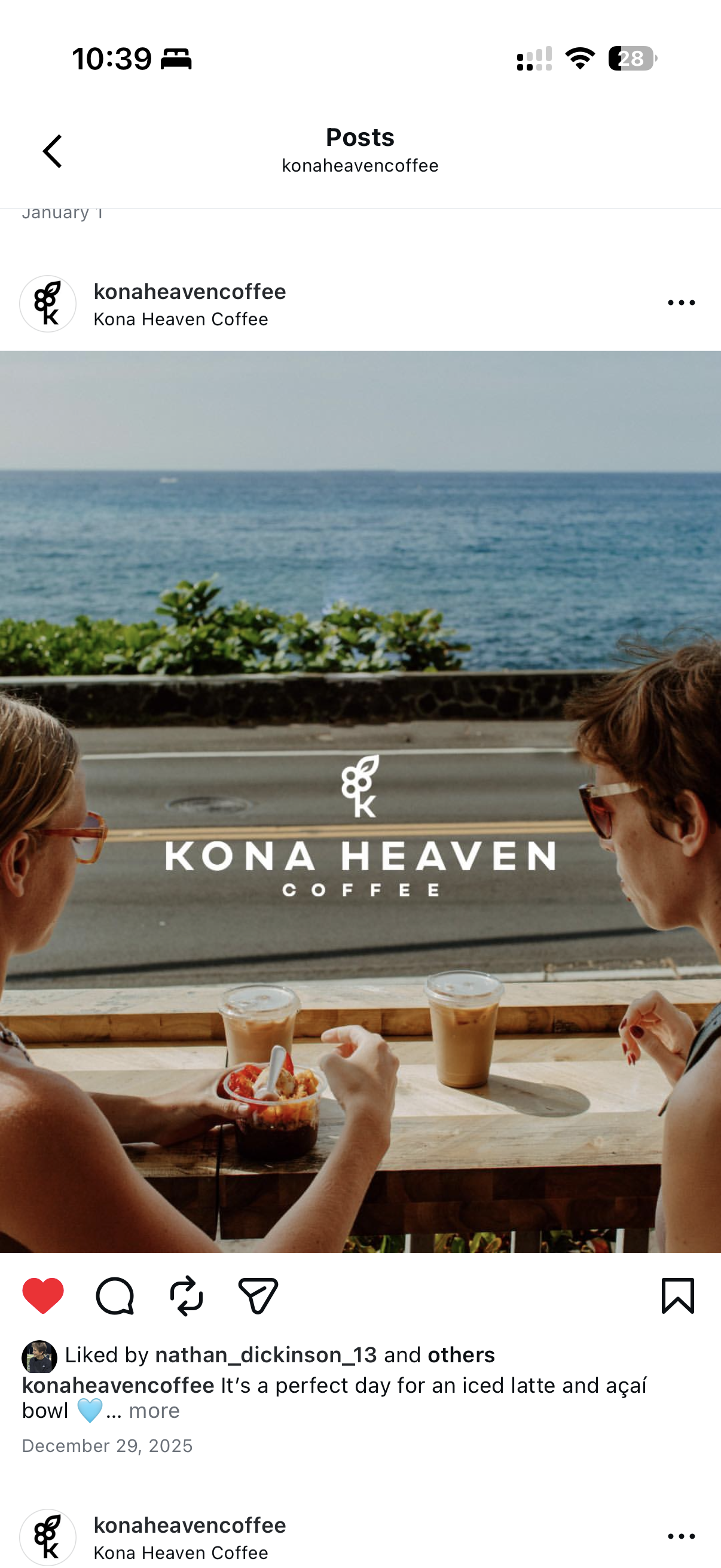 Two women sitting at an outdoor table overlooking the ocean, with drinks and an acai bowl in front of them, in front of a large window with Kona Heaven Coffee logo.