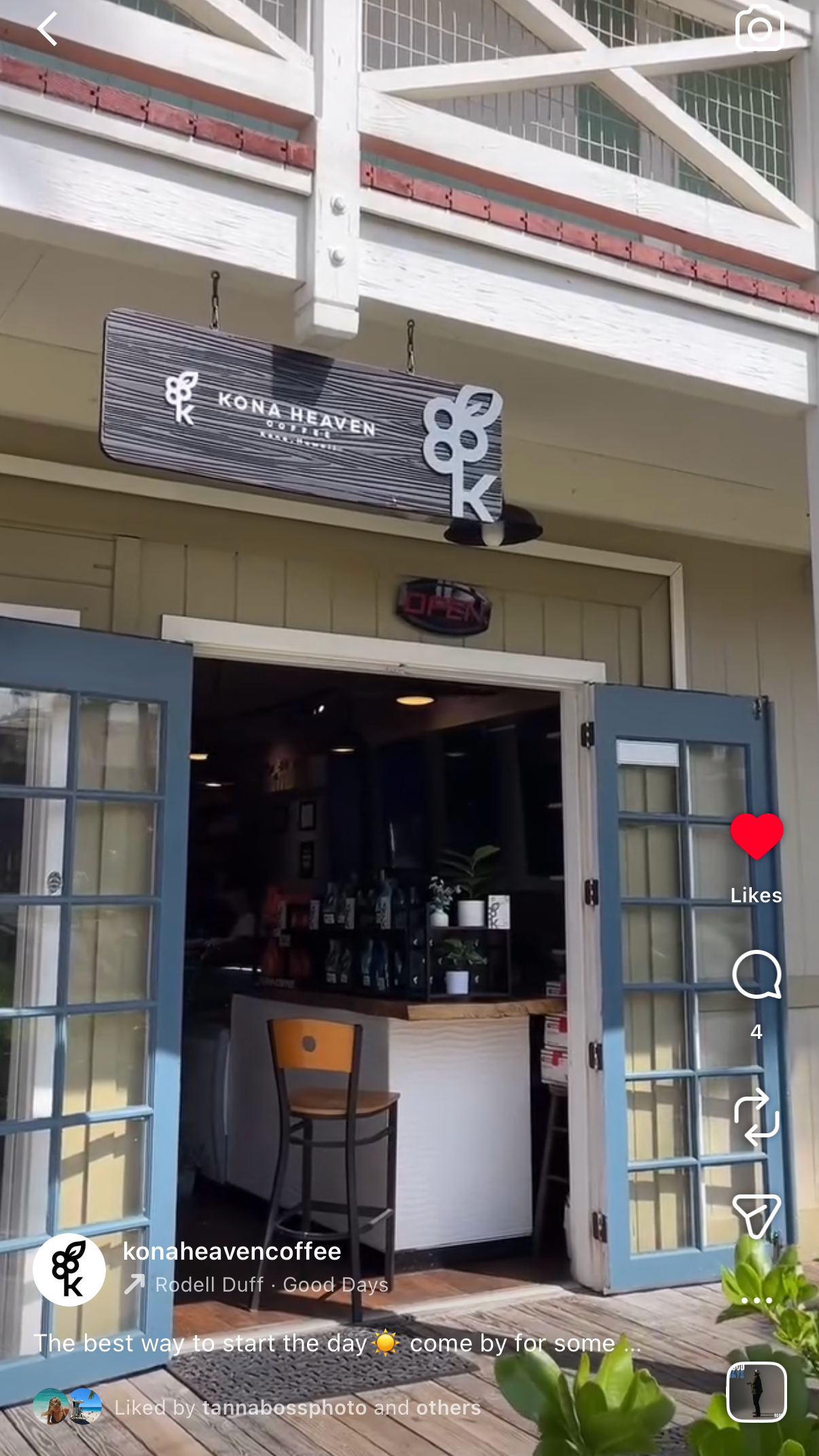 Exterior view of Kona Heaven Coffee shop with open blue double doors, signs reading 'Kona Heaven Coffee,' and an inside counter with plants and seating area.