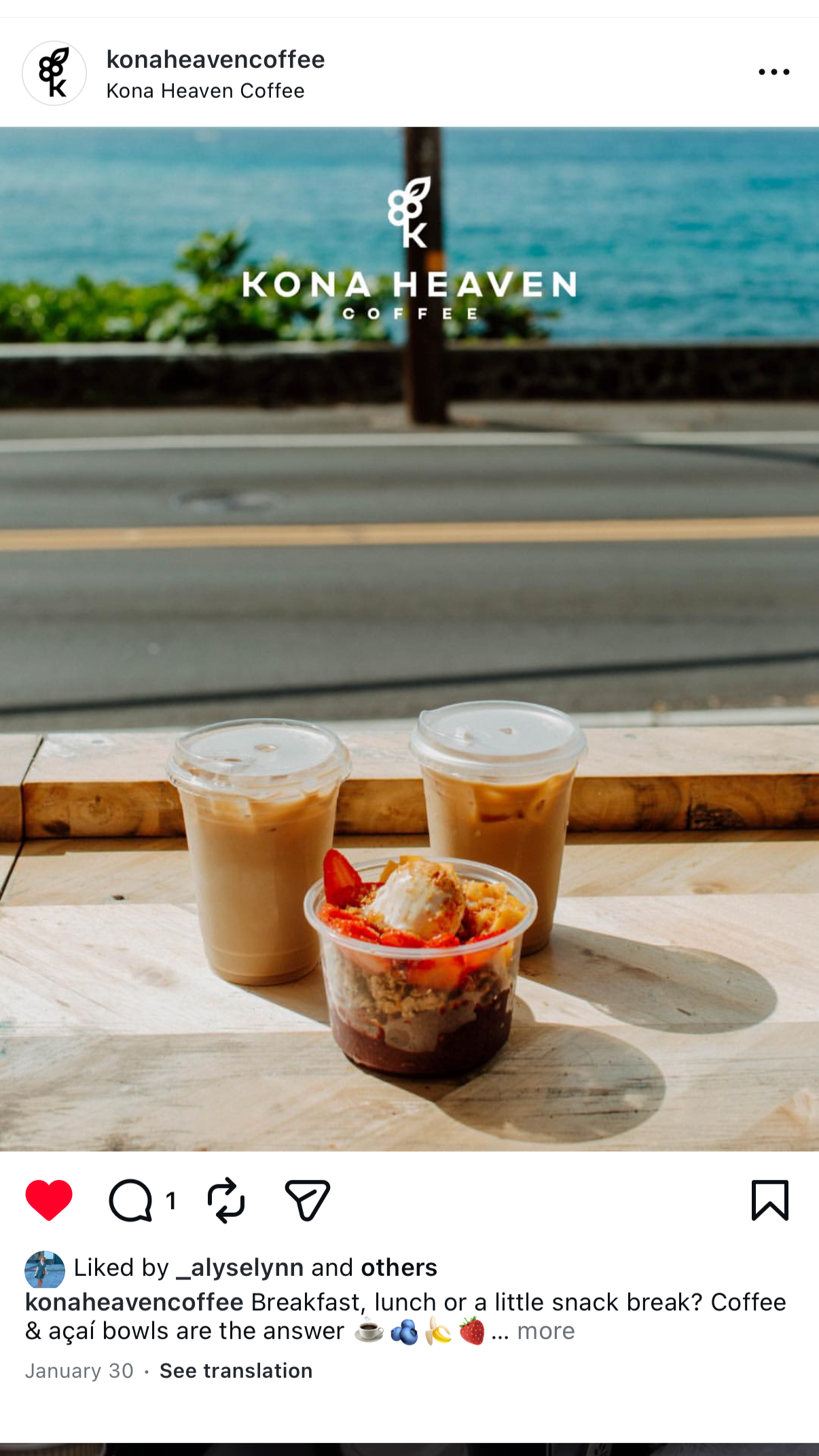 Two iced coffee drinks and a fruit and dessert bowl on a wooden table with a view of the ocean and street outside the window.