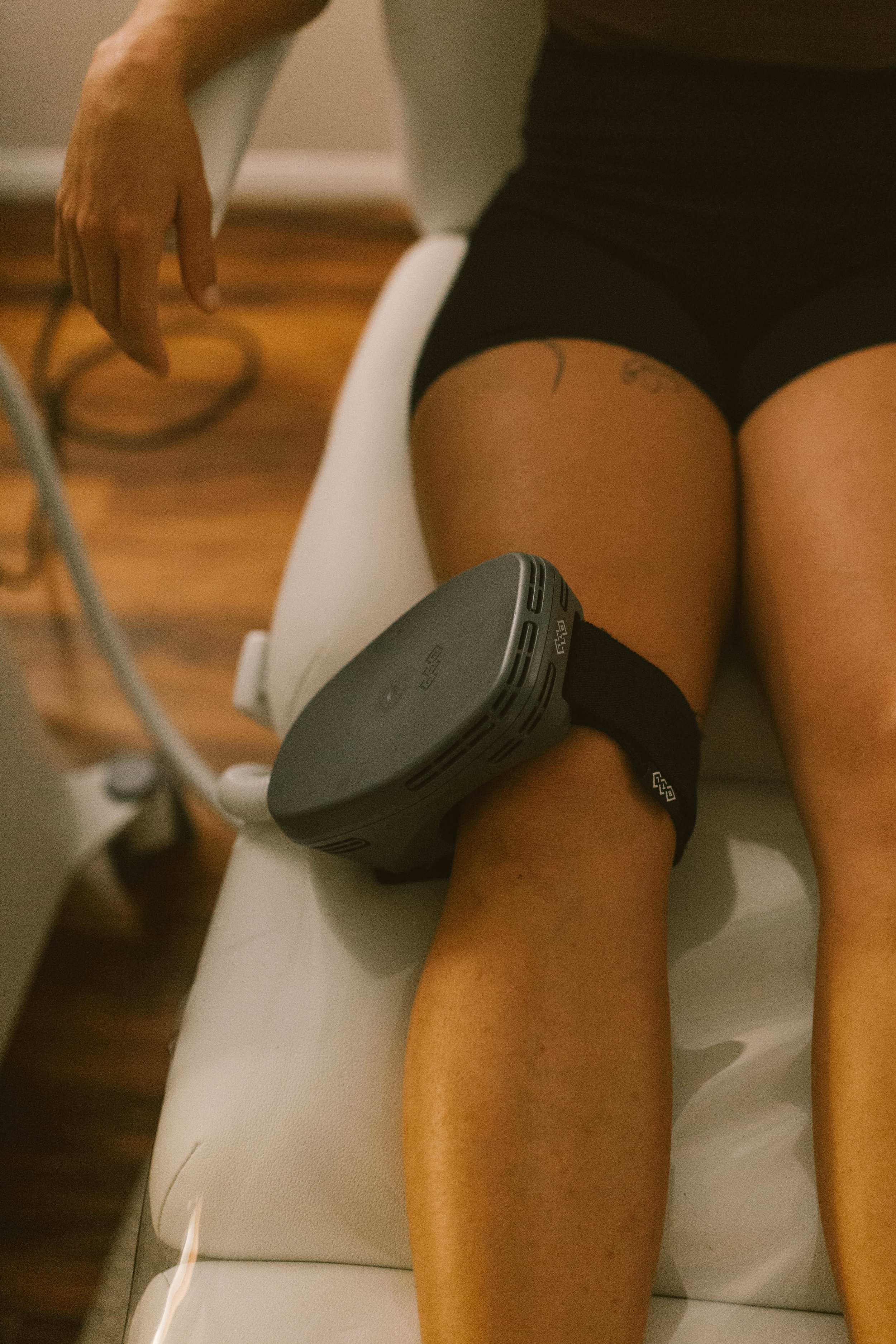 A person lying on their side on a medical examination table with a device around their thigh, likely during a medical test or procedure.
