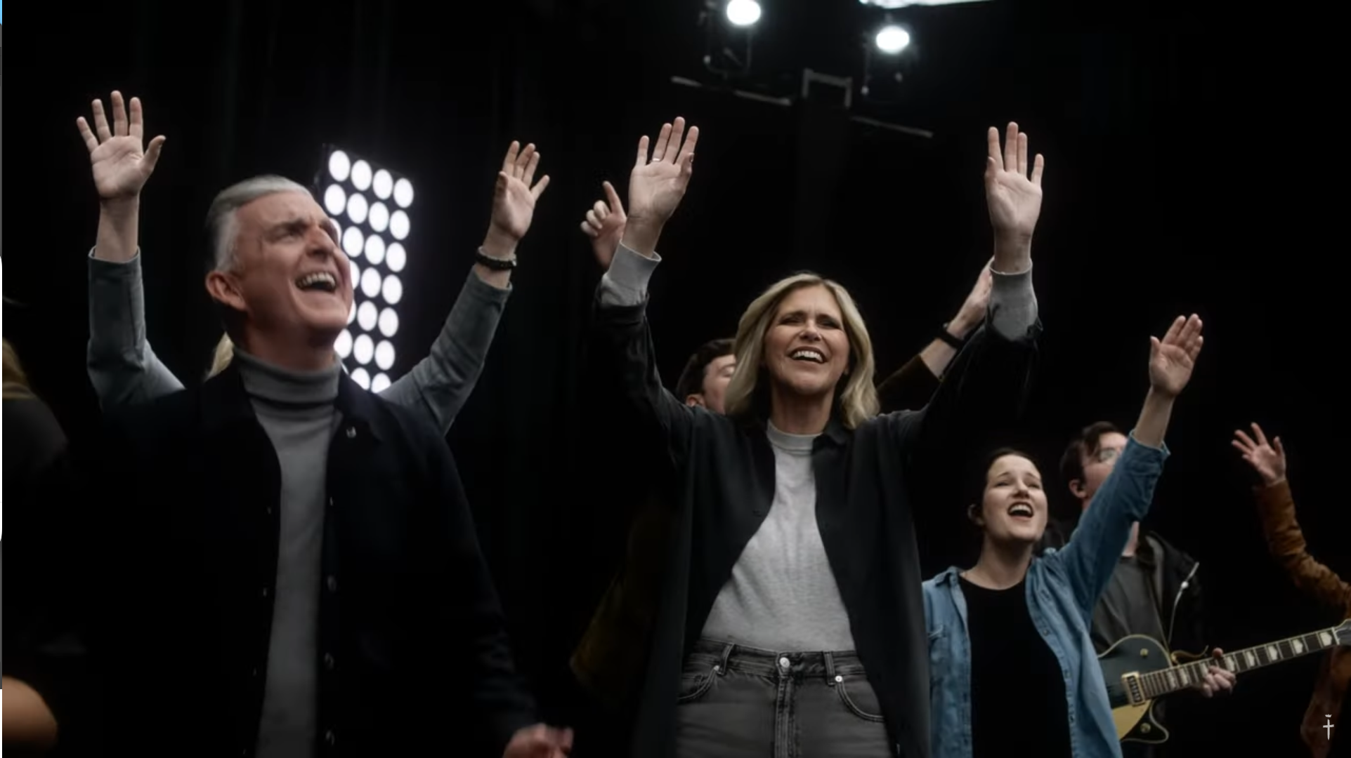 People worshiping with raised hands in a dark room illuminated by stage lights