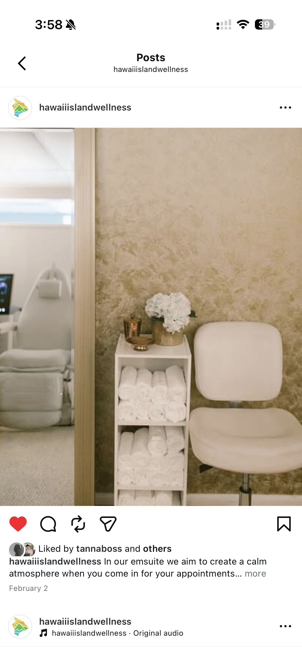 Spa or wellness treatment room with a cream-colored chair, a small white shelf with rolled white towels and a flower arrangement, and a beige wall in the background.