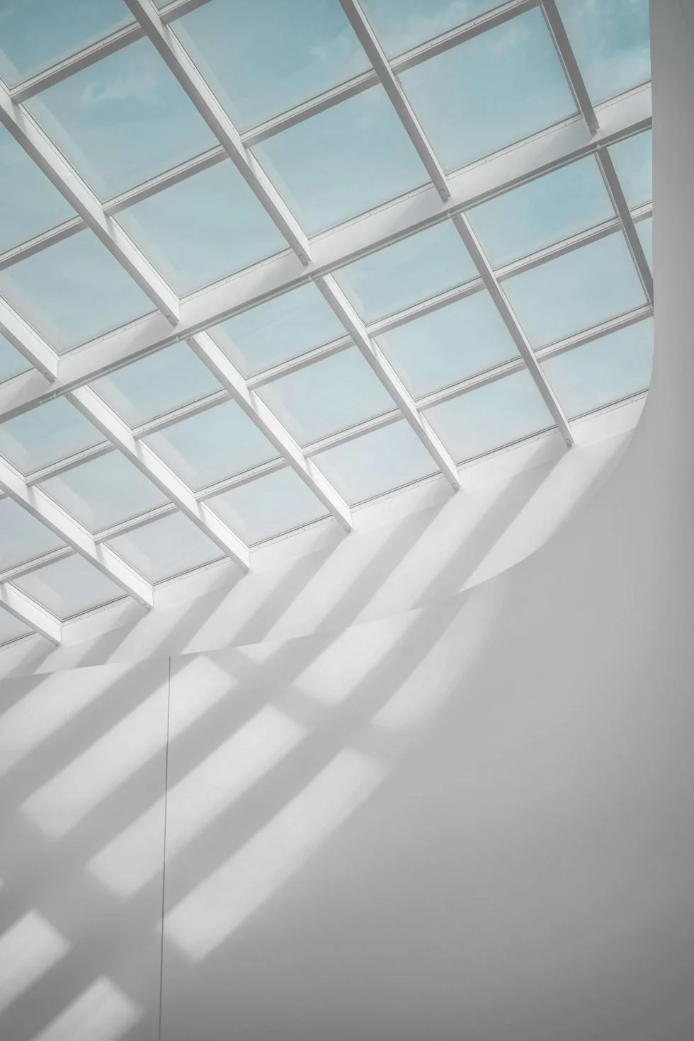 A skylight with multiple glass panels and white metal framing, casting shadows on a white wall below.