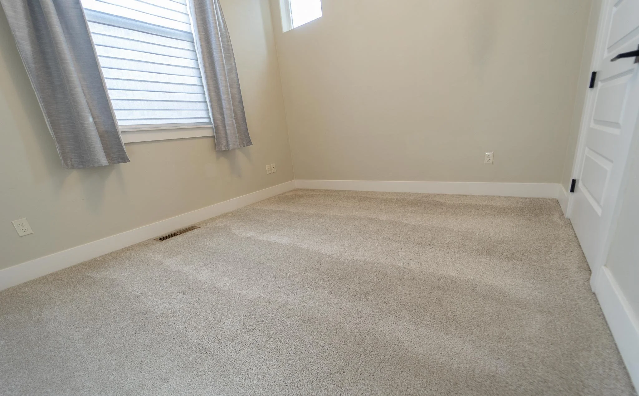 Empty room with light carpet, gray curtains, and a white door
