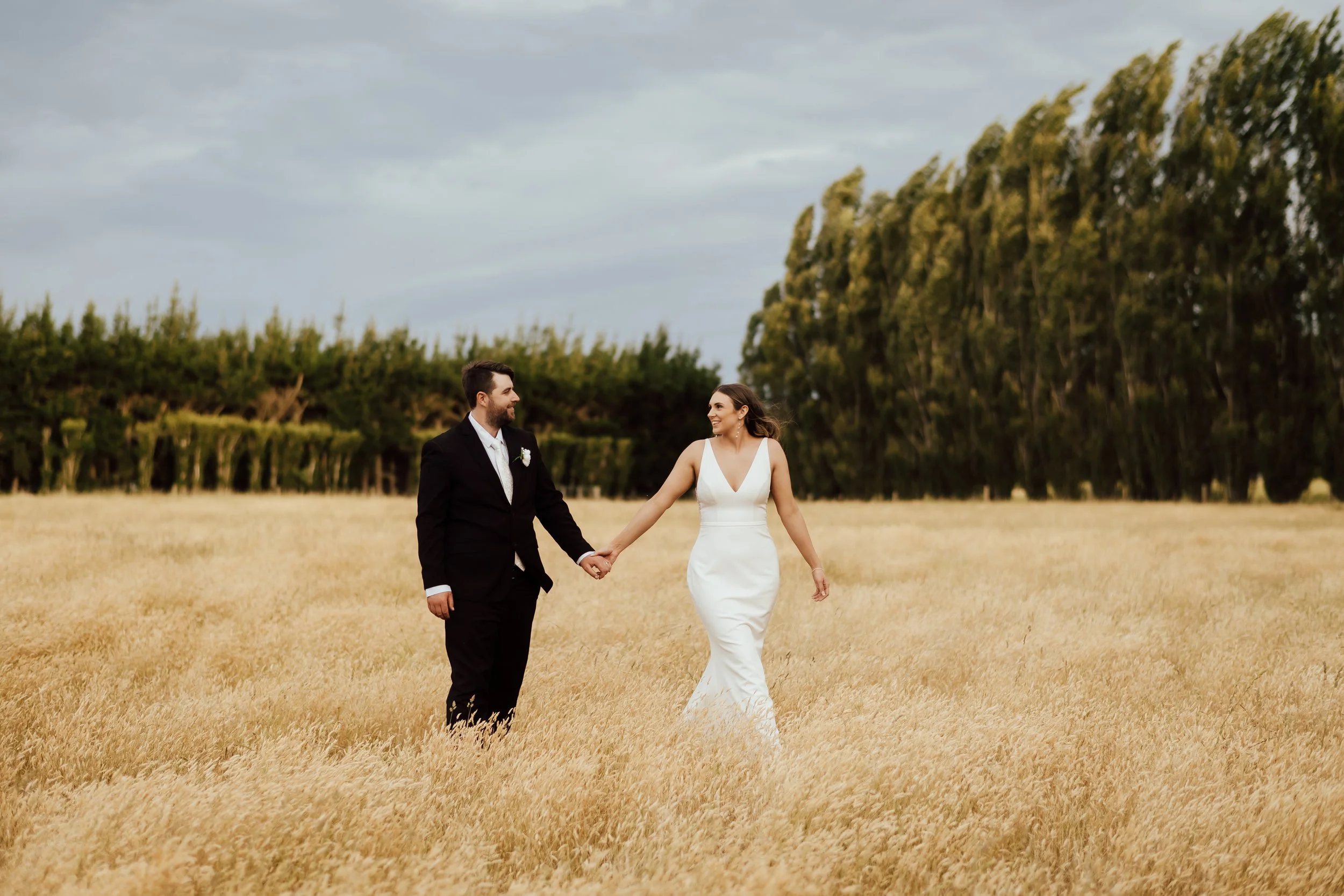 Bride and groom holding hands in long grass from Lucy and Caleb's wedding at Larcomb Vineyard photographed by Tracey Allsopp