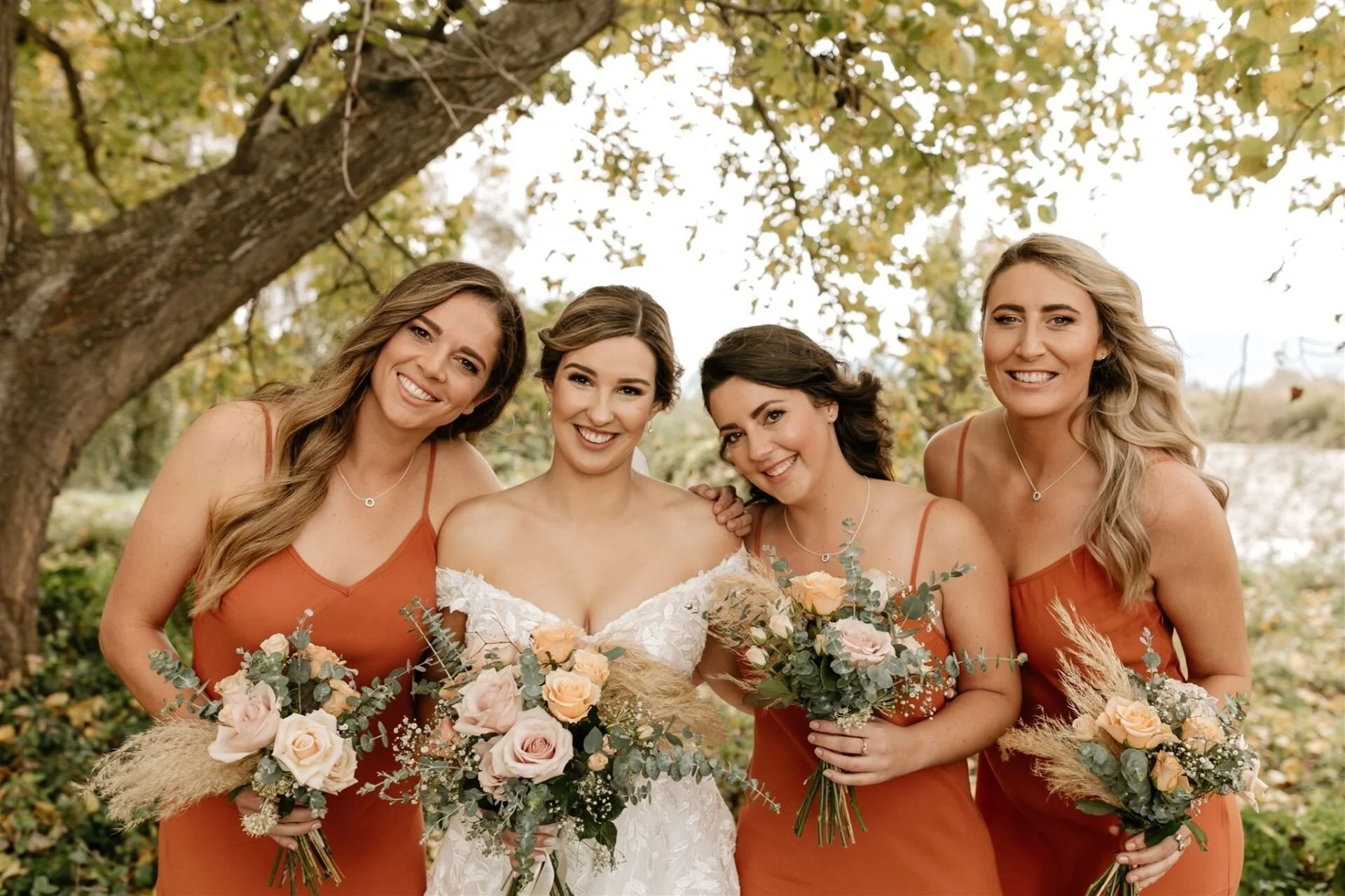 bridal party wearing copper coloured dresses and holding pastel rose bouquets under trees from Hannah & Jarel's wedding at Seifried Estate photographed by Renee Edwards Photography