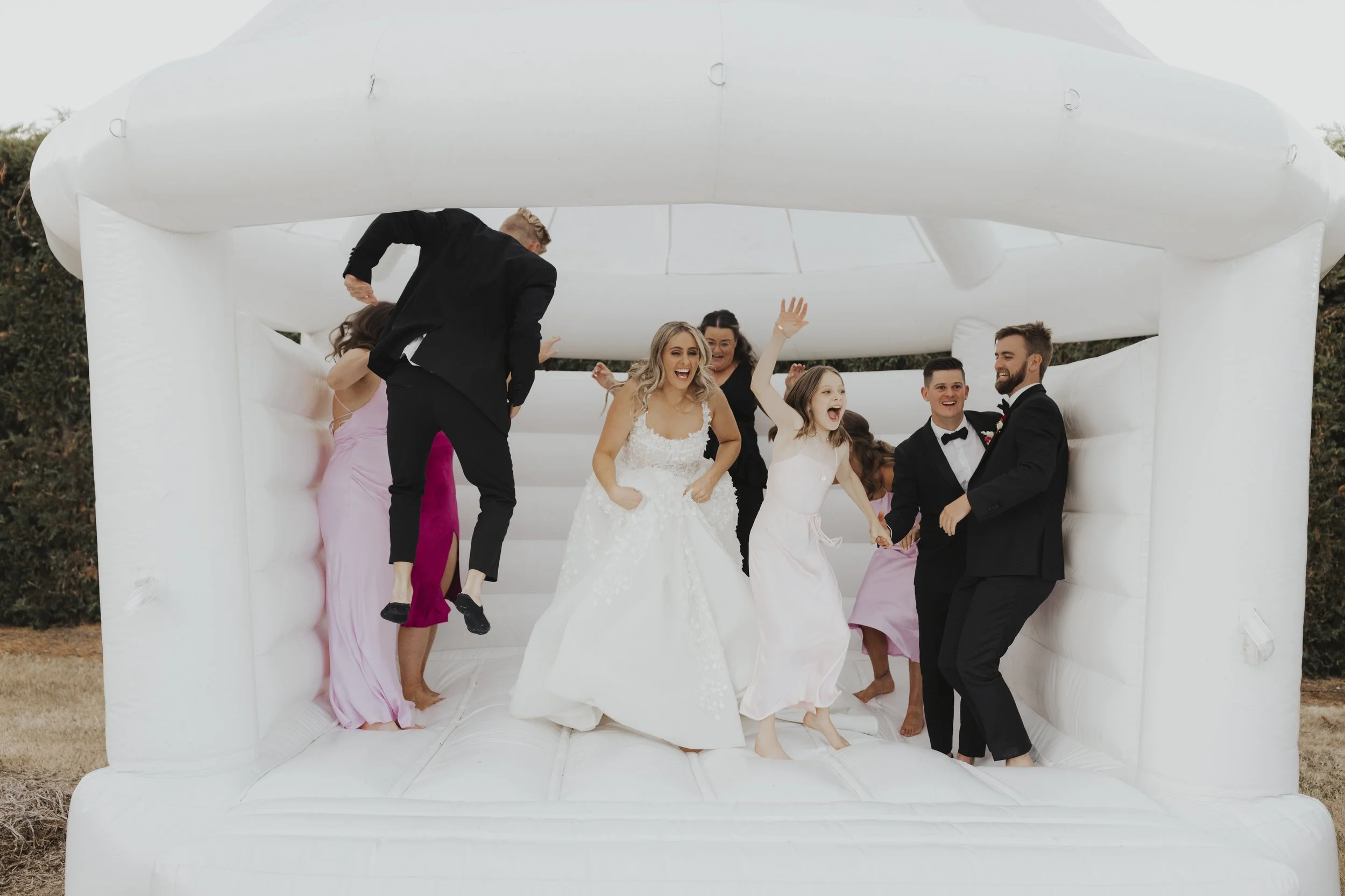 Wedding party jumping in a white bouncy castle from Kylie and Nick's wedding at a private home photographed by Sophie Isabella Photo