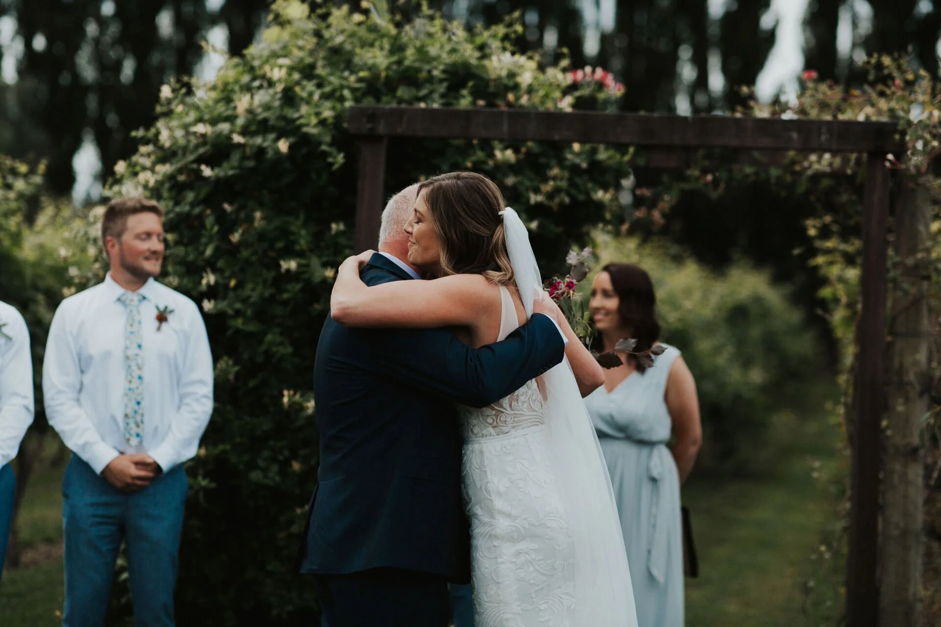 bride hugging family member in front of rose pergola from Jen & Lewis's wedding at Cossars Wineshed at Tai Tapu photographed by Sophie Isabella Photo
