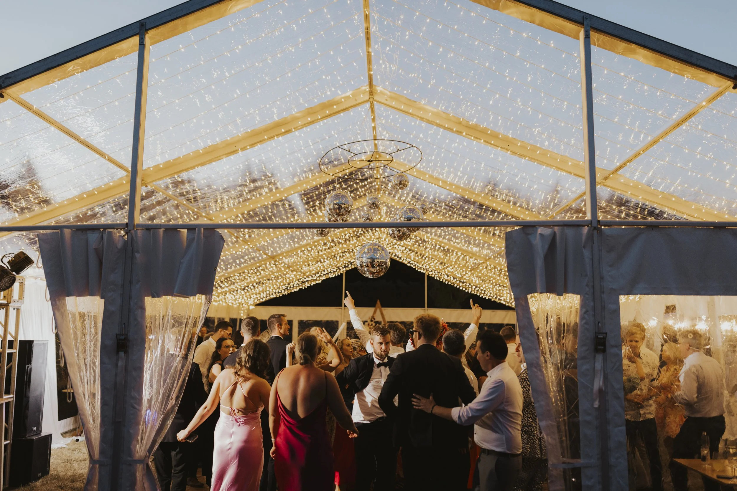 wedding guests dancing under mirrored disco balls in a clear marquee with fairy lights from Kylie and Nick's wedding at a private home photographed by Sophie Isabella Photo
