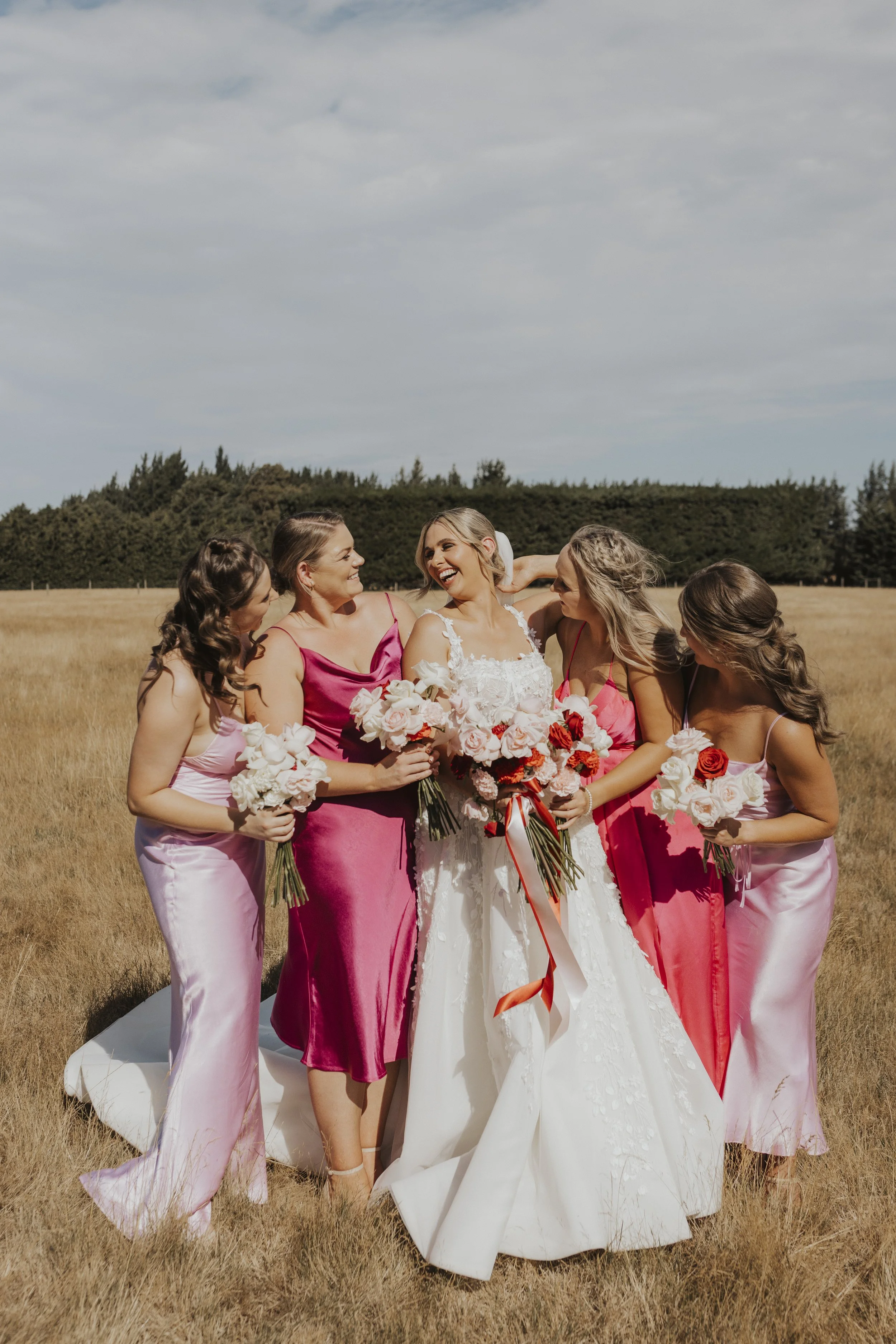 Bridal party laughing with bridesmaids wearing different coloured dresses from Kylie and Nick's wedding at a golden field photographed by Sophie Isabella Photo