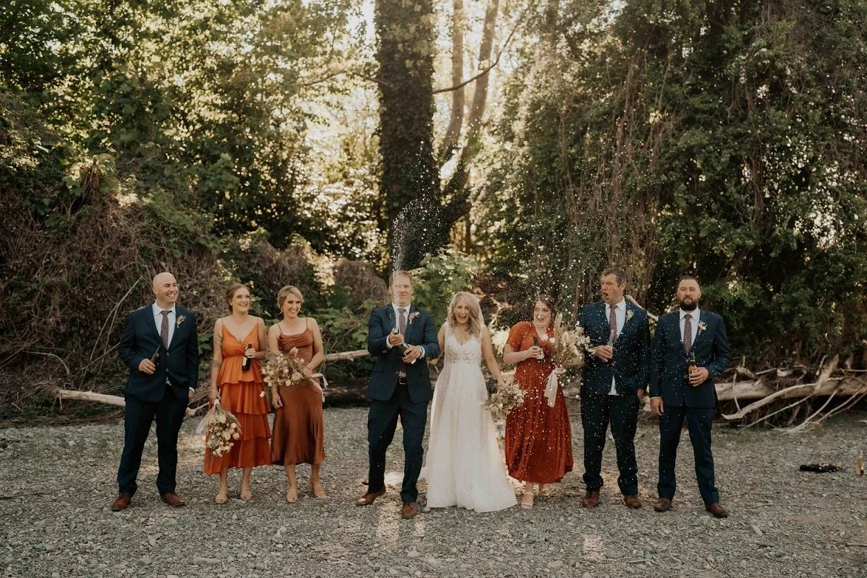 Wedding party with champagne spray on riverbank from Kirsty & Cameron's wedding at Stonebridge photographed by Sarah Clements Photography