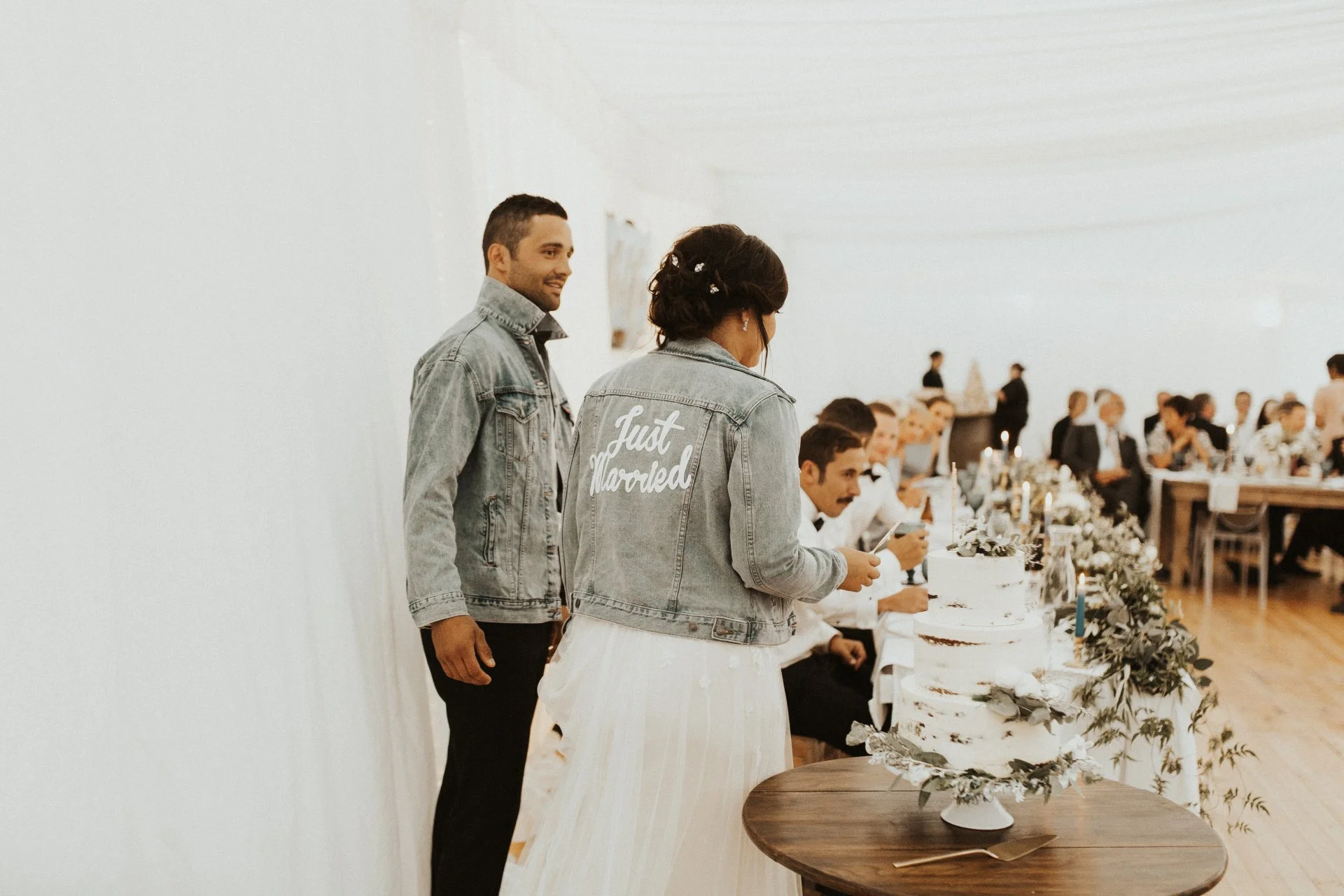 bride and groom wearing customised denim jackets while cutting wedding cake from Charlotte & Byron's wedding at Trott’s Garden photographed by Charlotte Sowman Photography
