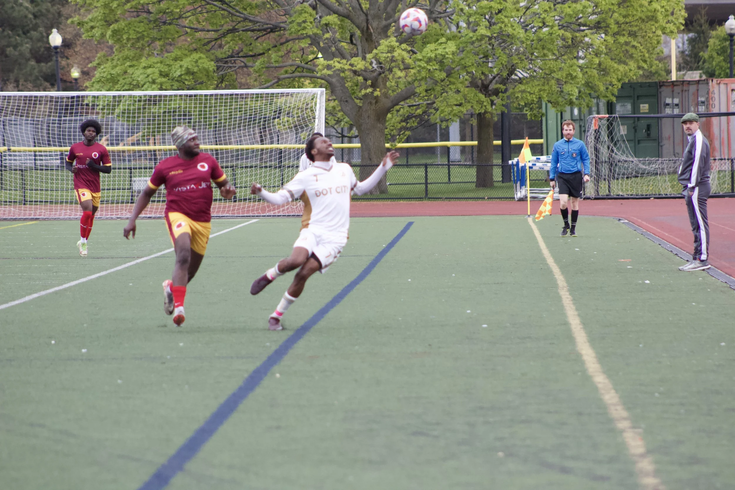 Soccer players and a referee on a field with a soccer ball in mid-air during a game.