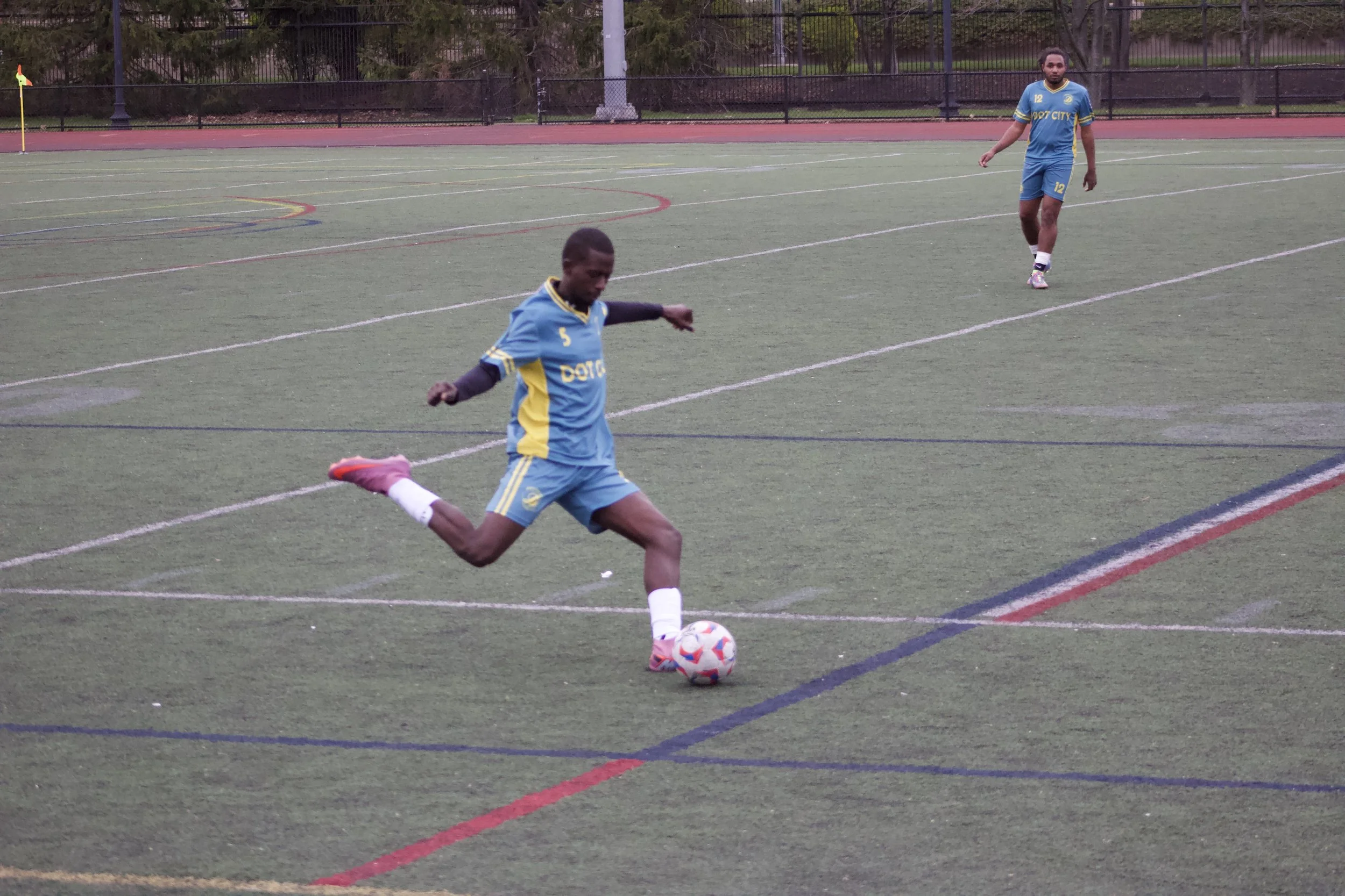 Soccer players wearing blue and yellow jerseys practicing on a synthetic turf field.