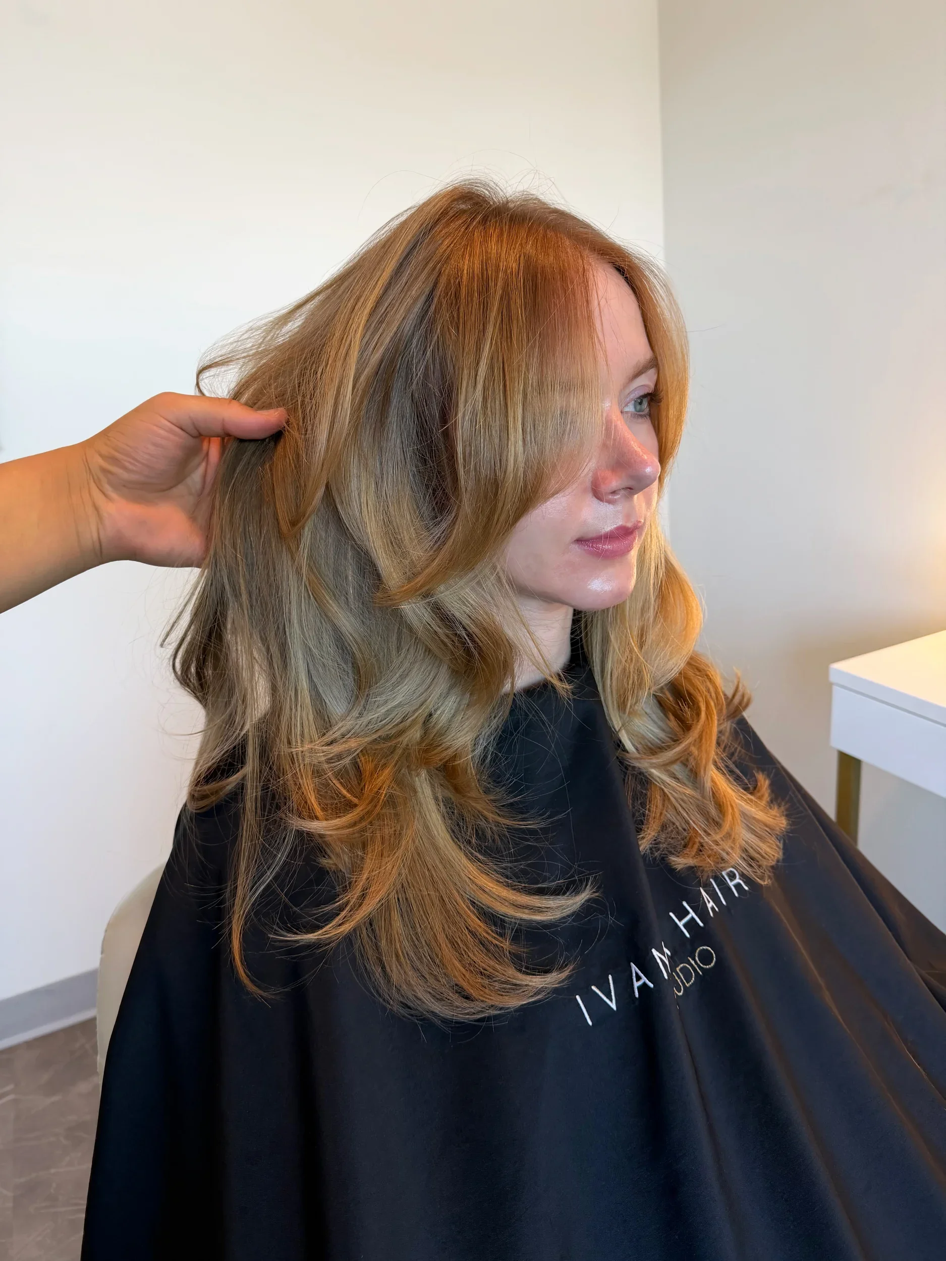 A three-quarter profile view of a butterfly haircut with curtain bangs and a voluminous bombshell blowout on honey blonde hair, styled by Ivan at Ivan X Hair in Kennewick, WA.⁠