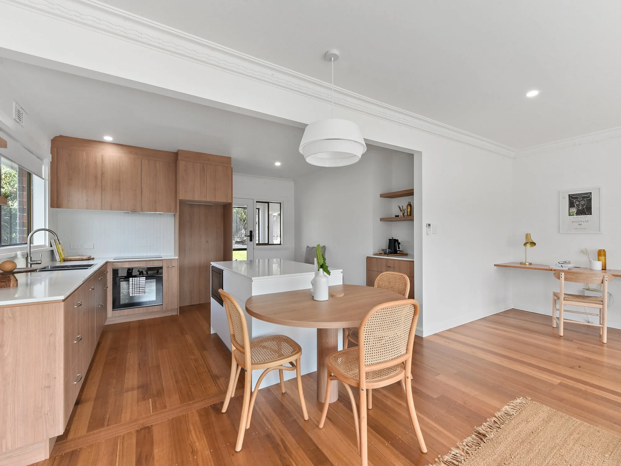 an open kitchen with warm white and timber tones, a table attached to an island bench.