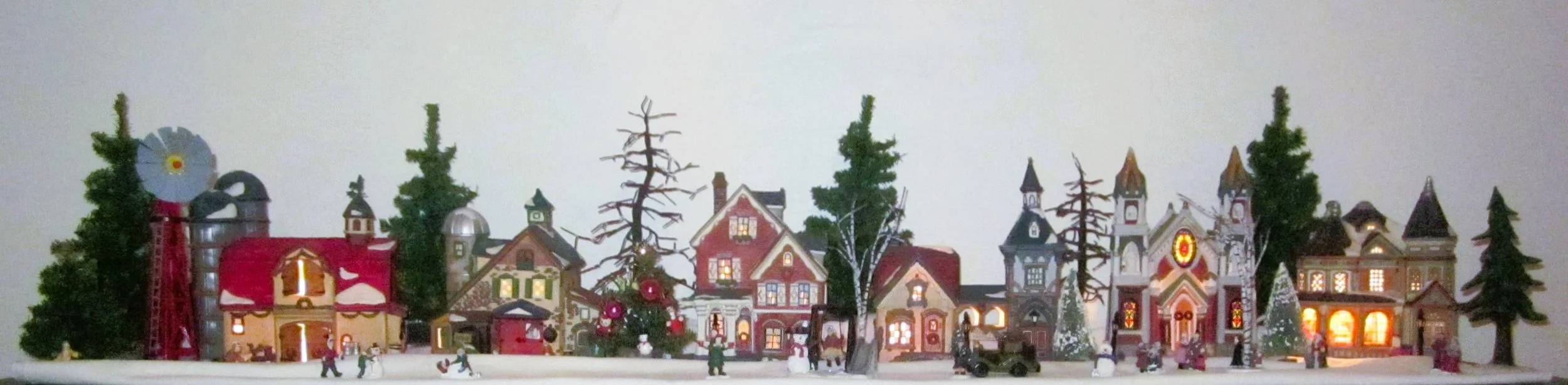 Miniature Christmas village with decorated houses, trees, and figures, illuminated from within, set on a snowy landscape.