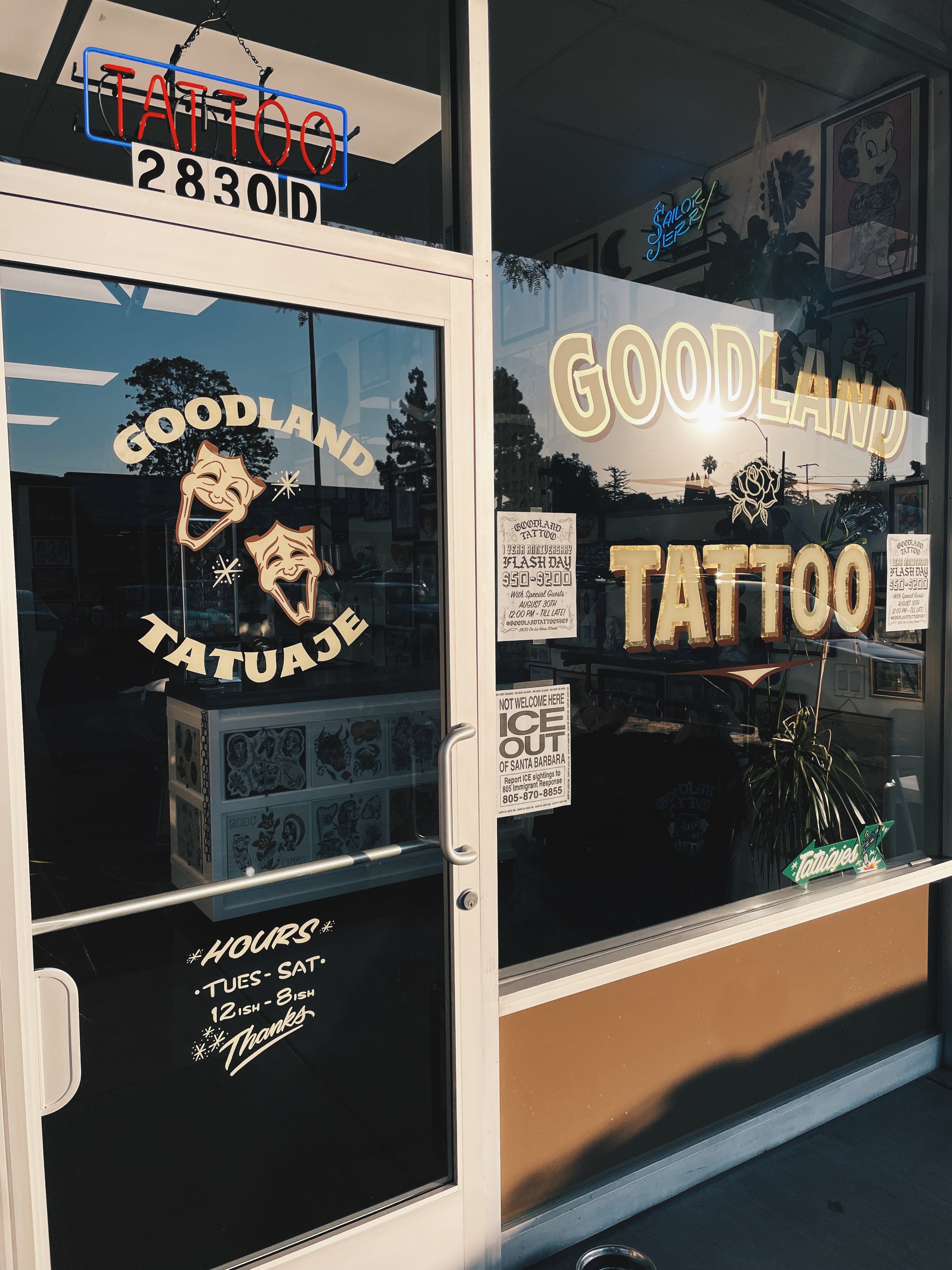 The image shows the glass door of a tattoo shop with the words 'Goodland Tattoo' written in paint.