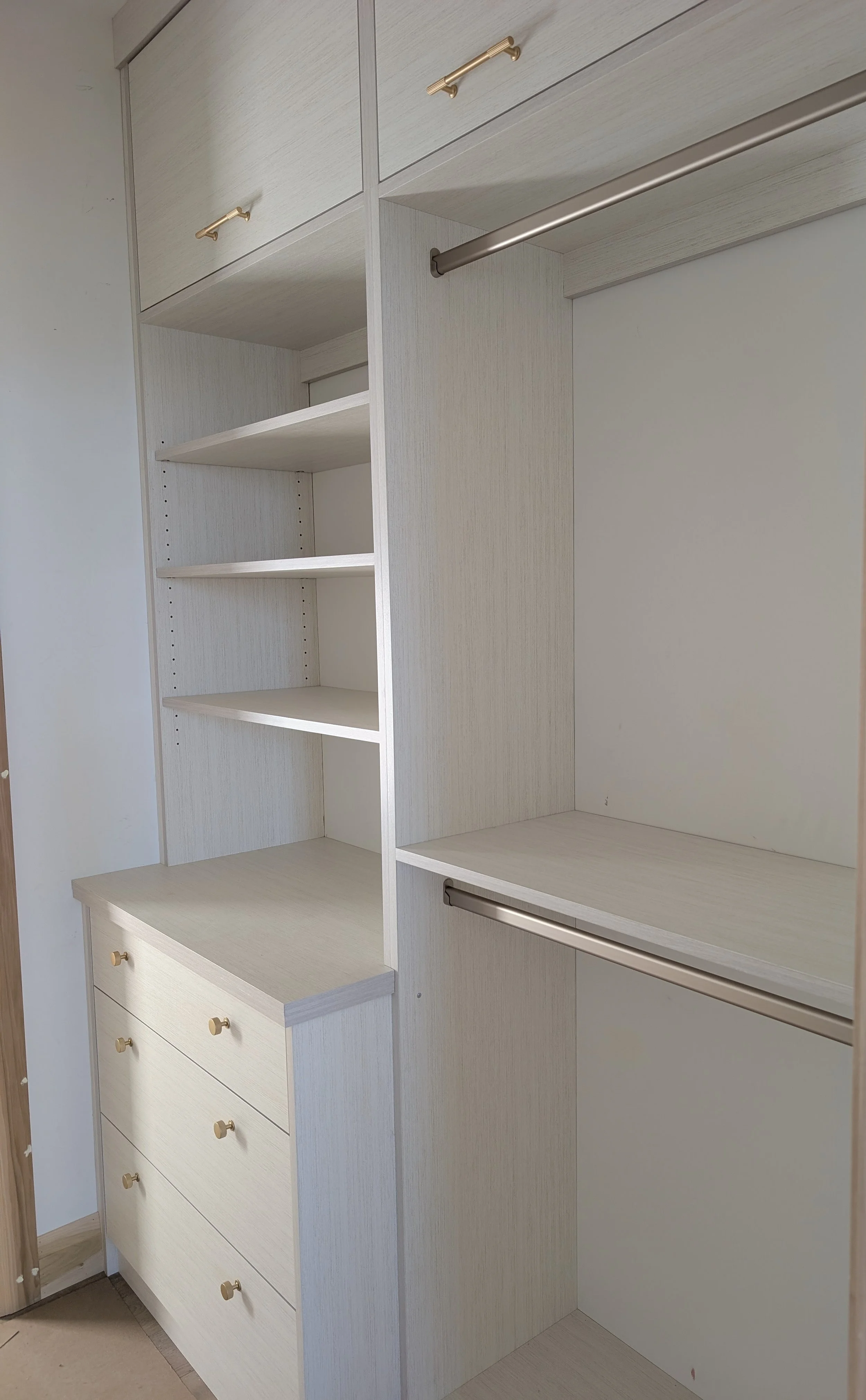 Empty built-in closet with white shelves, drawers, and metal rods for hanging clothes.