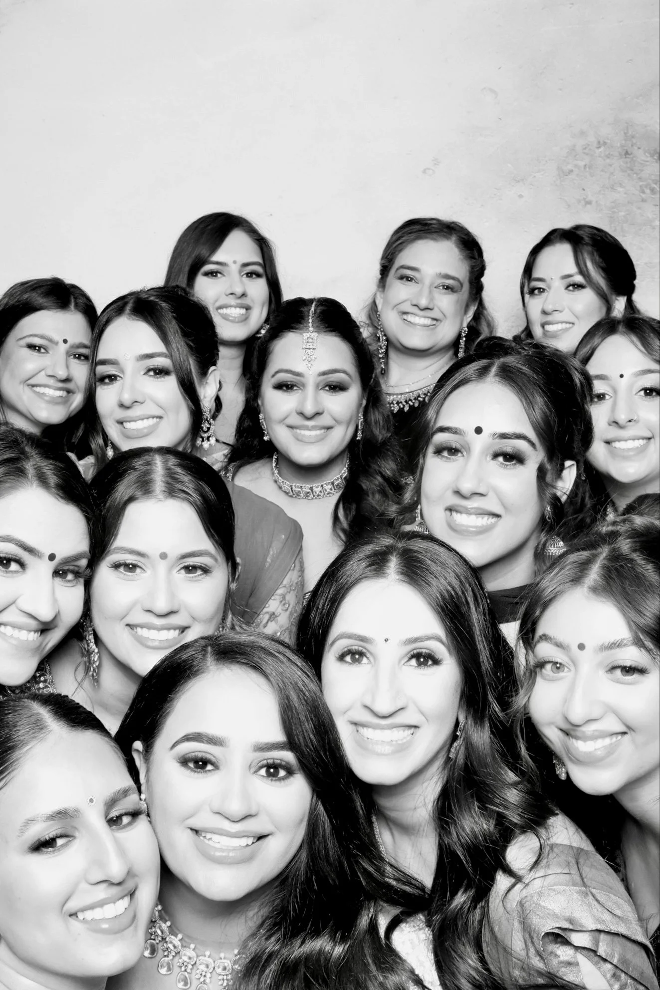 Group of women smiling, dressed in traditional Indian attire with jewelry, in a black and white photo.