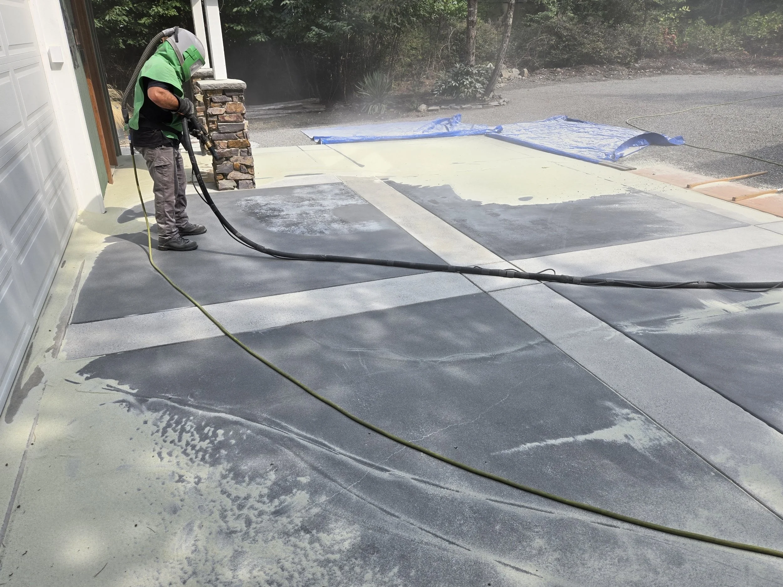 Sand blasted a concrete driveway near a garage and porch, stripped selant,  and a blue tarp in the background.