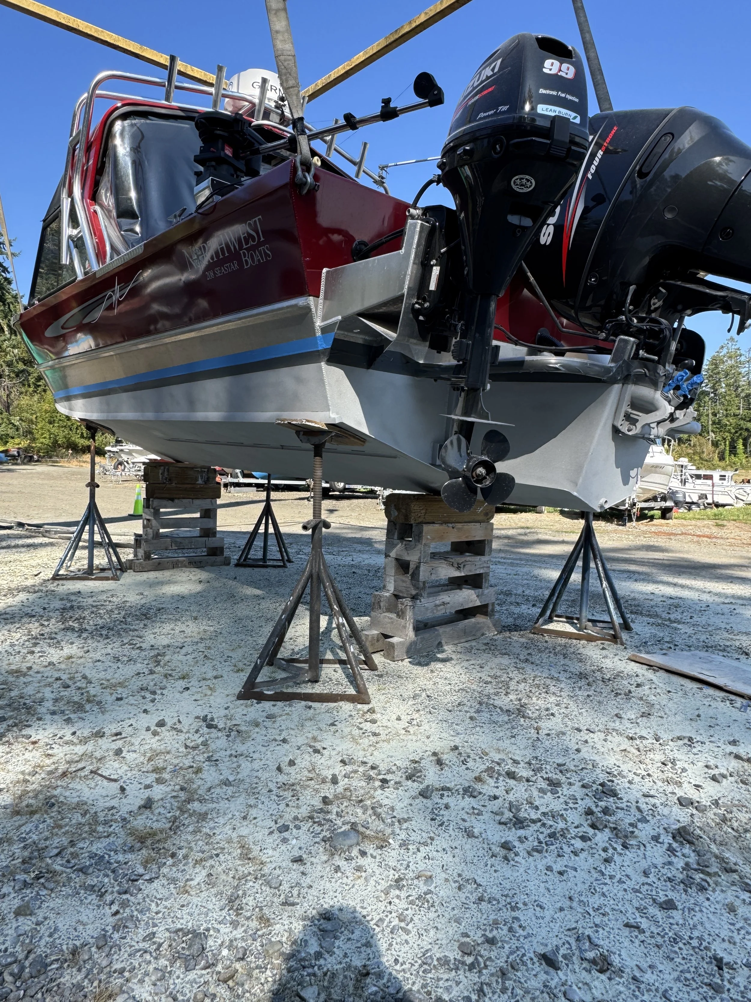 Sand Blasted A boat, it is elevated on wooden blocks and metal supports in a boatyard, with a clear blue sky in the background.
