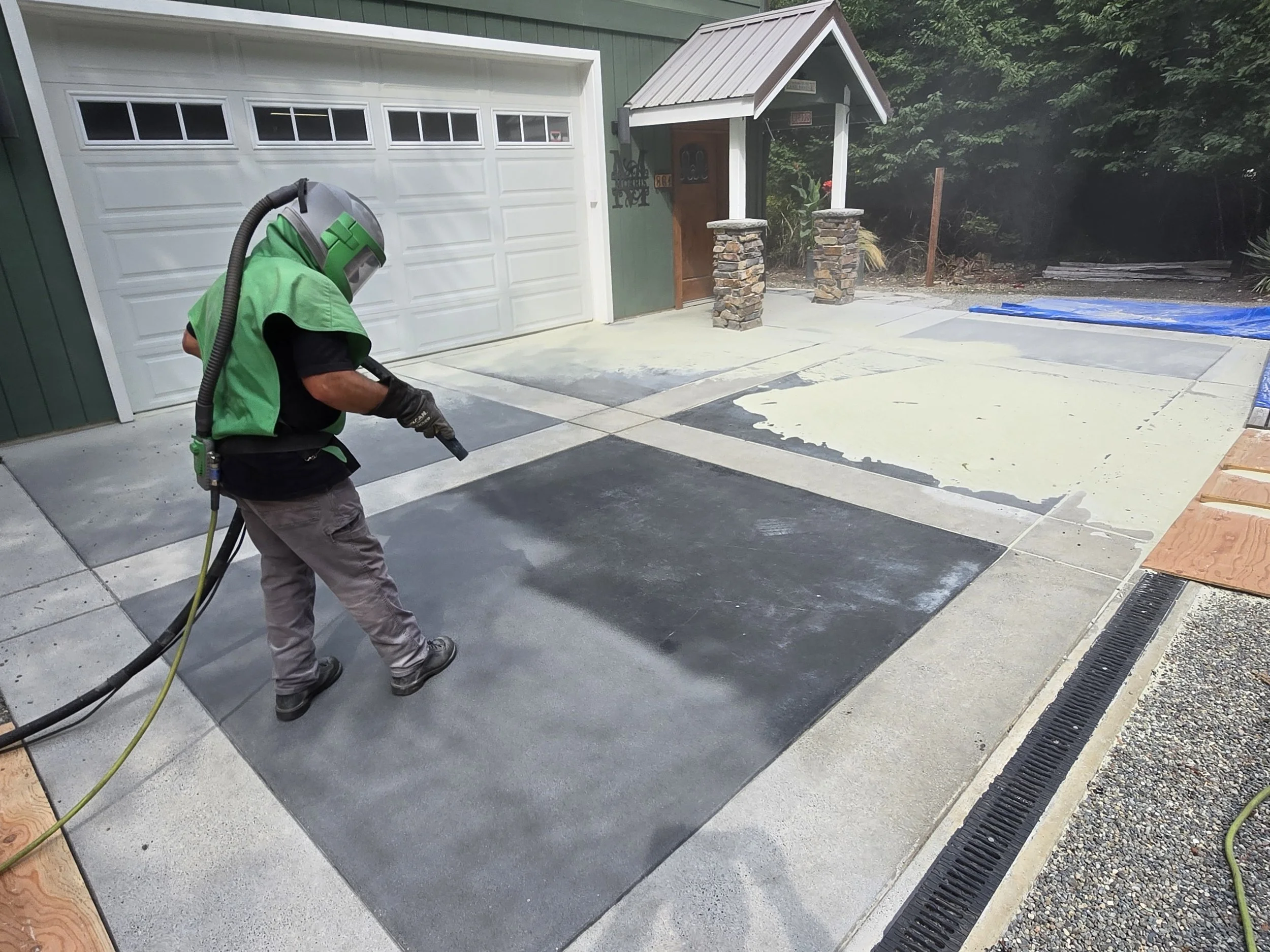 sand blasting sealant from  a concrete driveway in front of a house with a garage door.