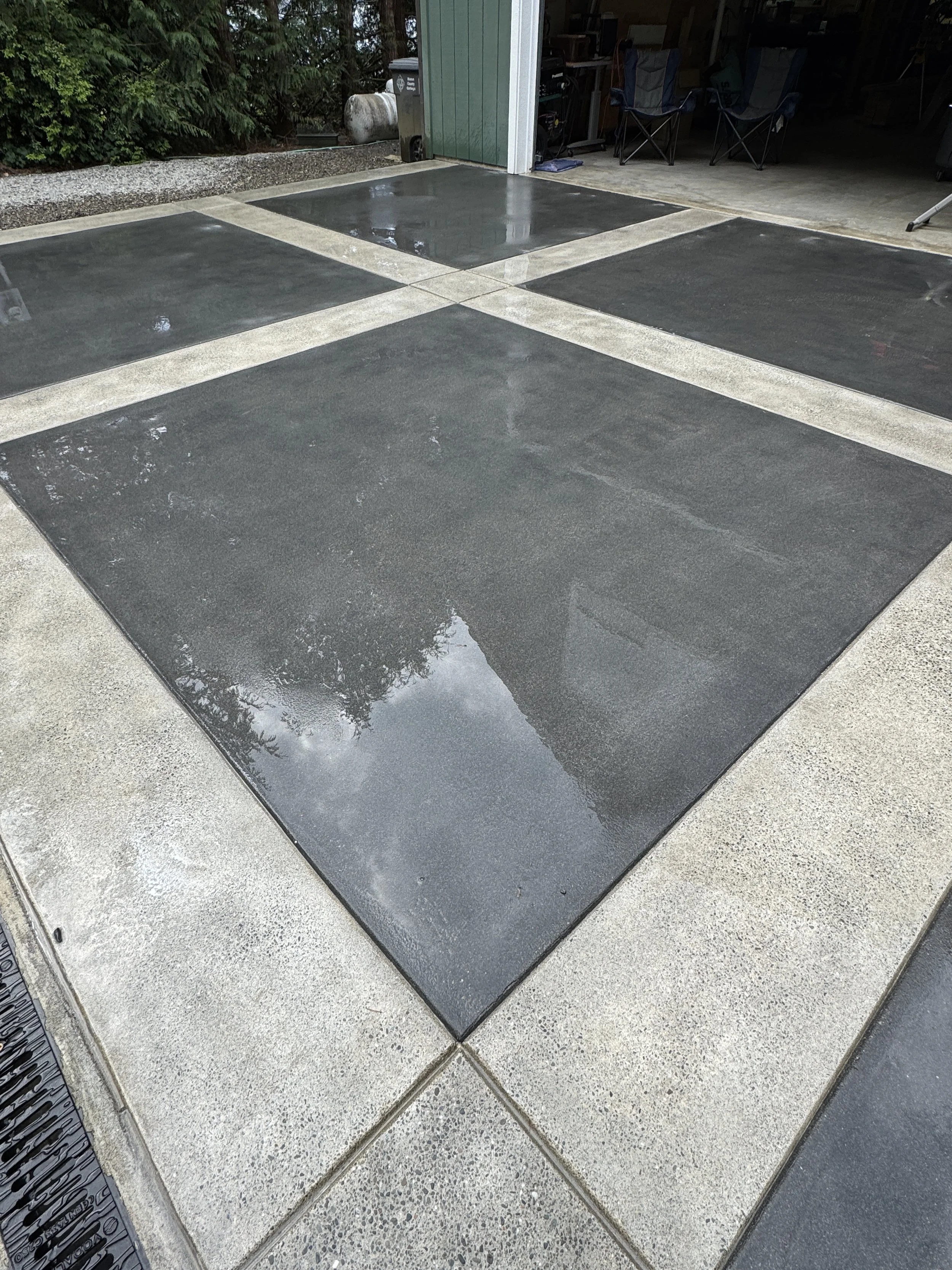 Wet sand blasted concrete driveway with black and gray sections in front of a garage.