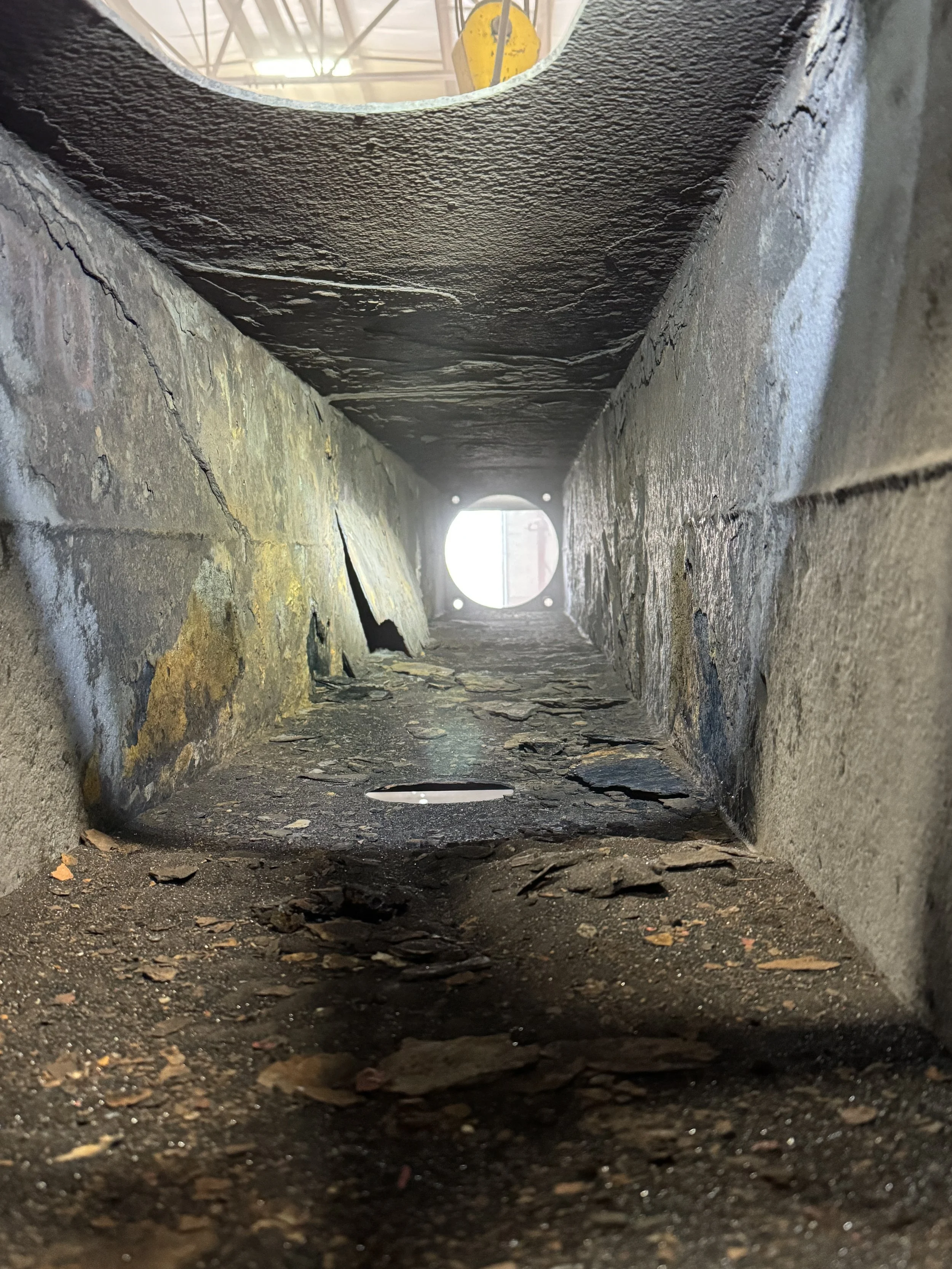 Sand blasting and Looking through a rectangular vent or pipe with chipped and weathered edges, dirt and debris inside, and a light source at the end.