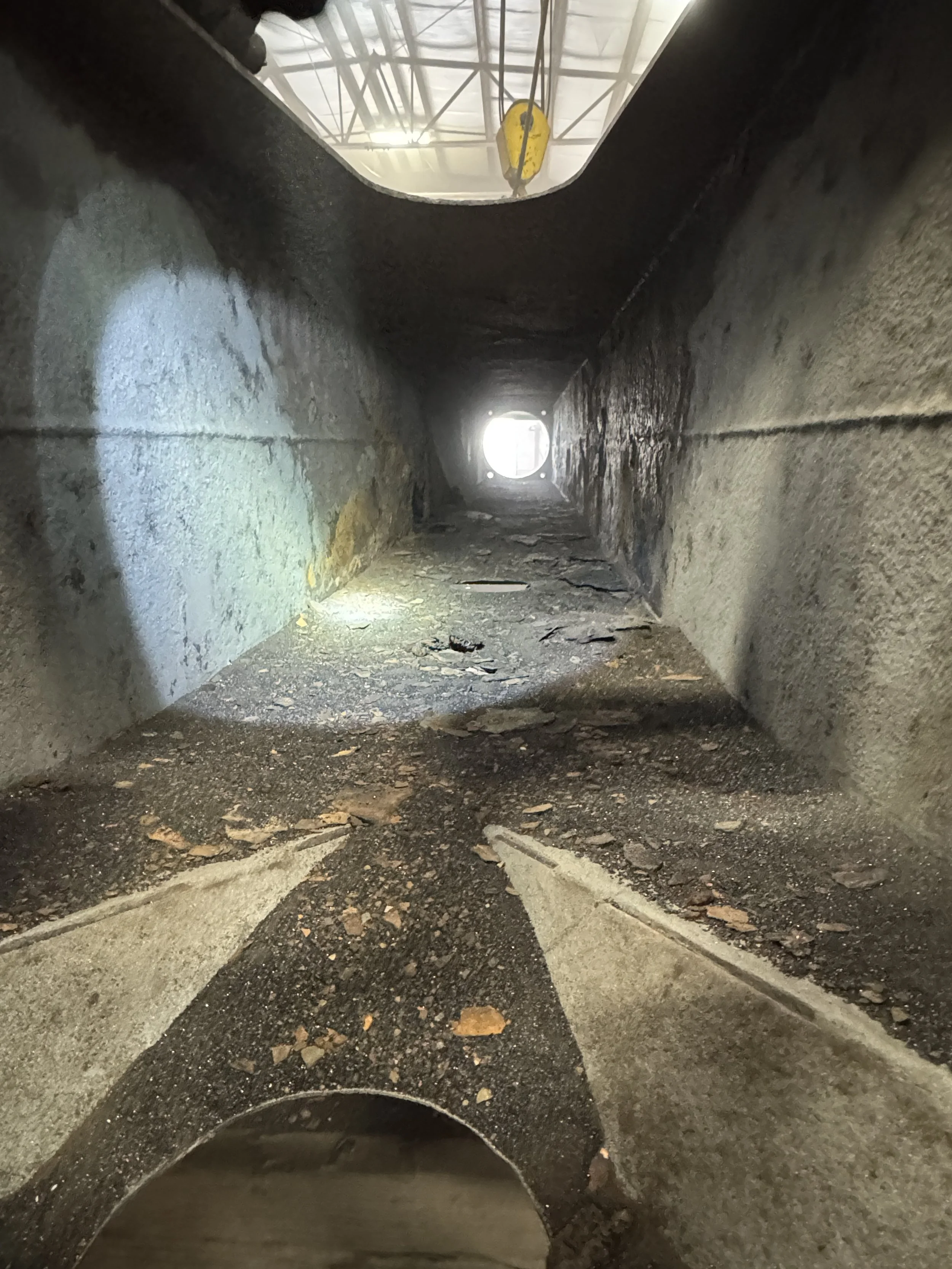 sand blasting Inside a narrow industrial metal pipe or duct with a rough interior, showing dirt and grime. Light from the outside is visible at the end of the pipe.