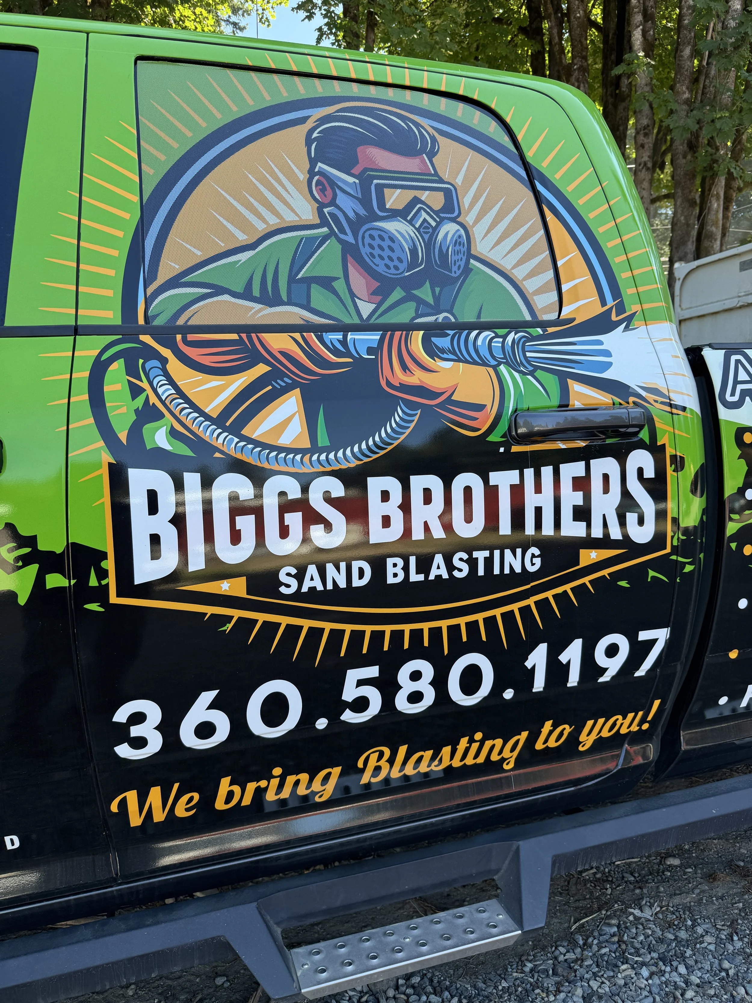 Graphic advertisement on a vehicle for Biggs Brothers Sand Blasting company, featuring a cartoon of a person wearing a goggles and a gas mask, holding a sandblasting hose, with contact information and slogan.