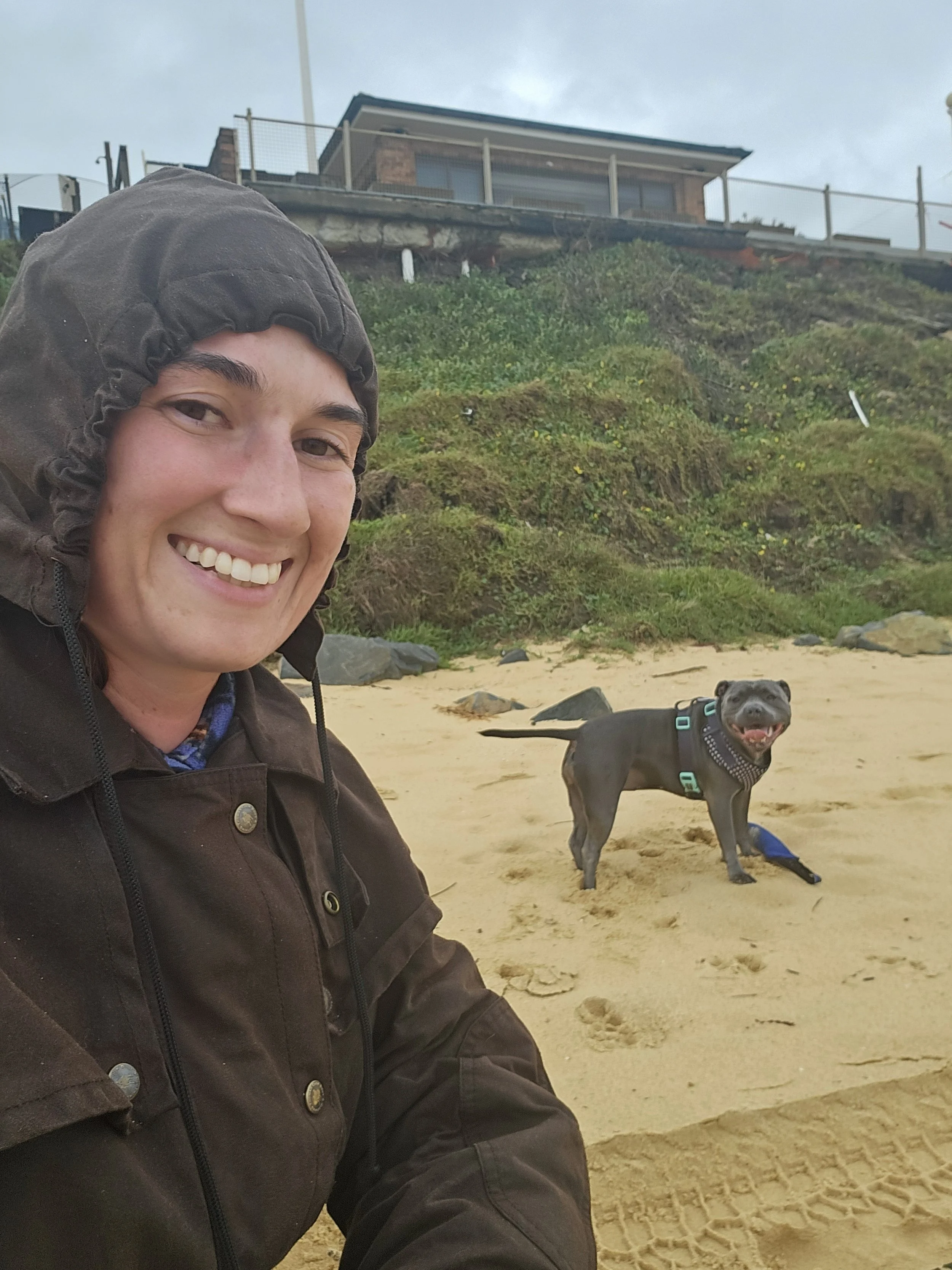 A selfie on the beach in the rain with a staffy smiling in the background