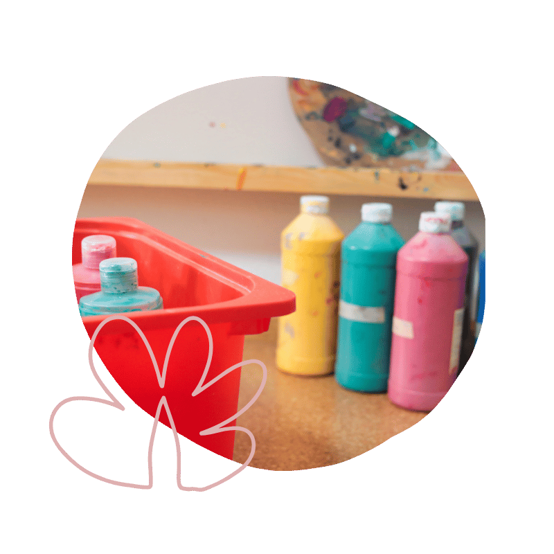 Farben zum Malen in Flaschen auf einem Tisch, neben einer roten Farbmischbox, in einem kreativen Raum.