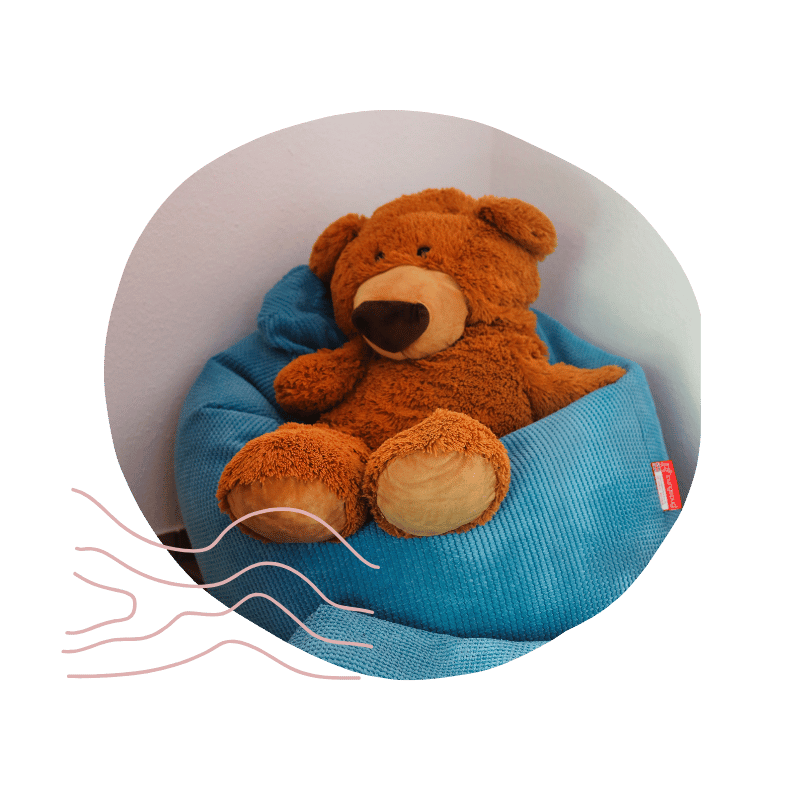 Plüschbär sitzt in einem blauen Sitzsack, vor weißer Wand.