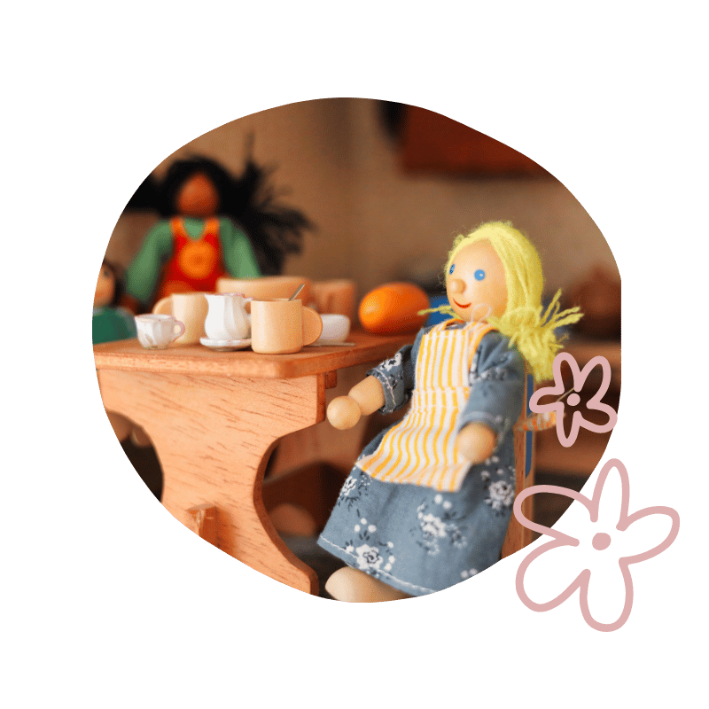 Spielzeugküche mit Puppen beim Spielen, including eine sitzende Puppe mit blonden Haaren und eine andere Puppe im Hintergrund