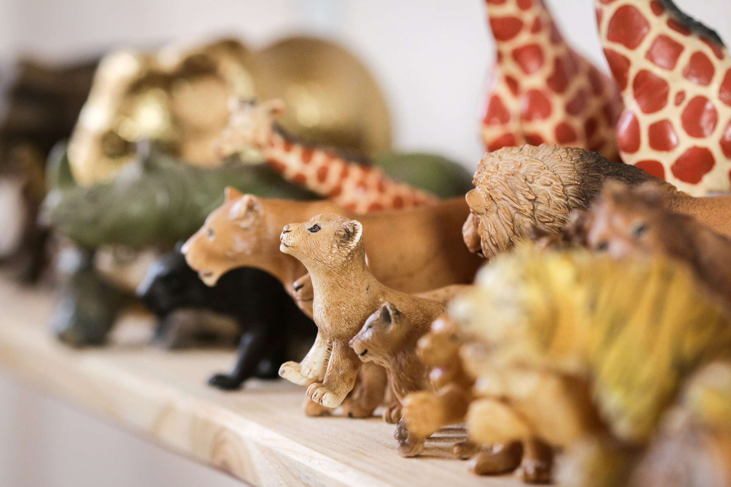 Verschiedene kleine Tierfiguren aus Holz auf einer Holzplatte, darunter Löwen, Giraffen, Löwen und andere Tiere.
