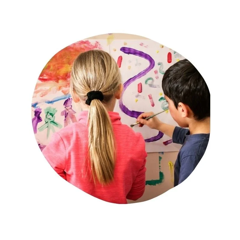 Zwei Kinder malen zusammen auf einem großen weißen Papier mit bunten Farben.