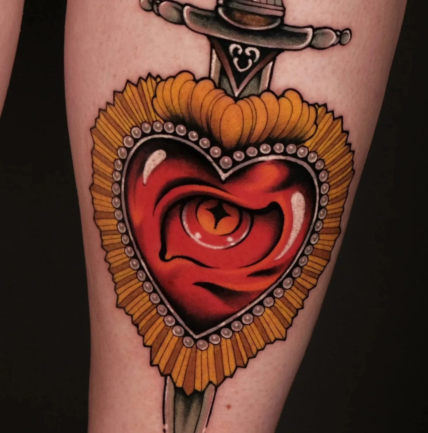 Traditional style tattoo of a heart with a face, surrounded by a sunflower and pearls, with a dagger behind it.