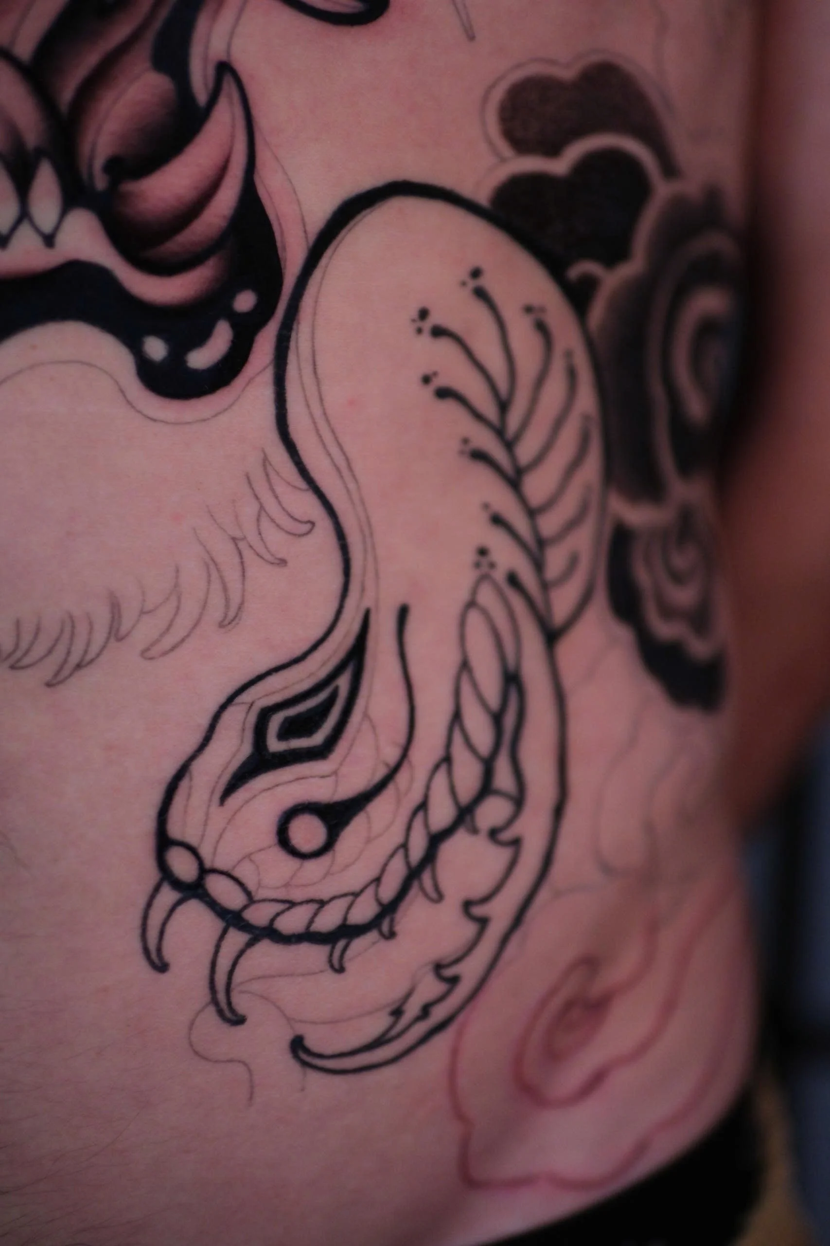 Close-up of a tattoo on skin featuring intricate black linework, including floral and abstract design elements.