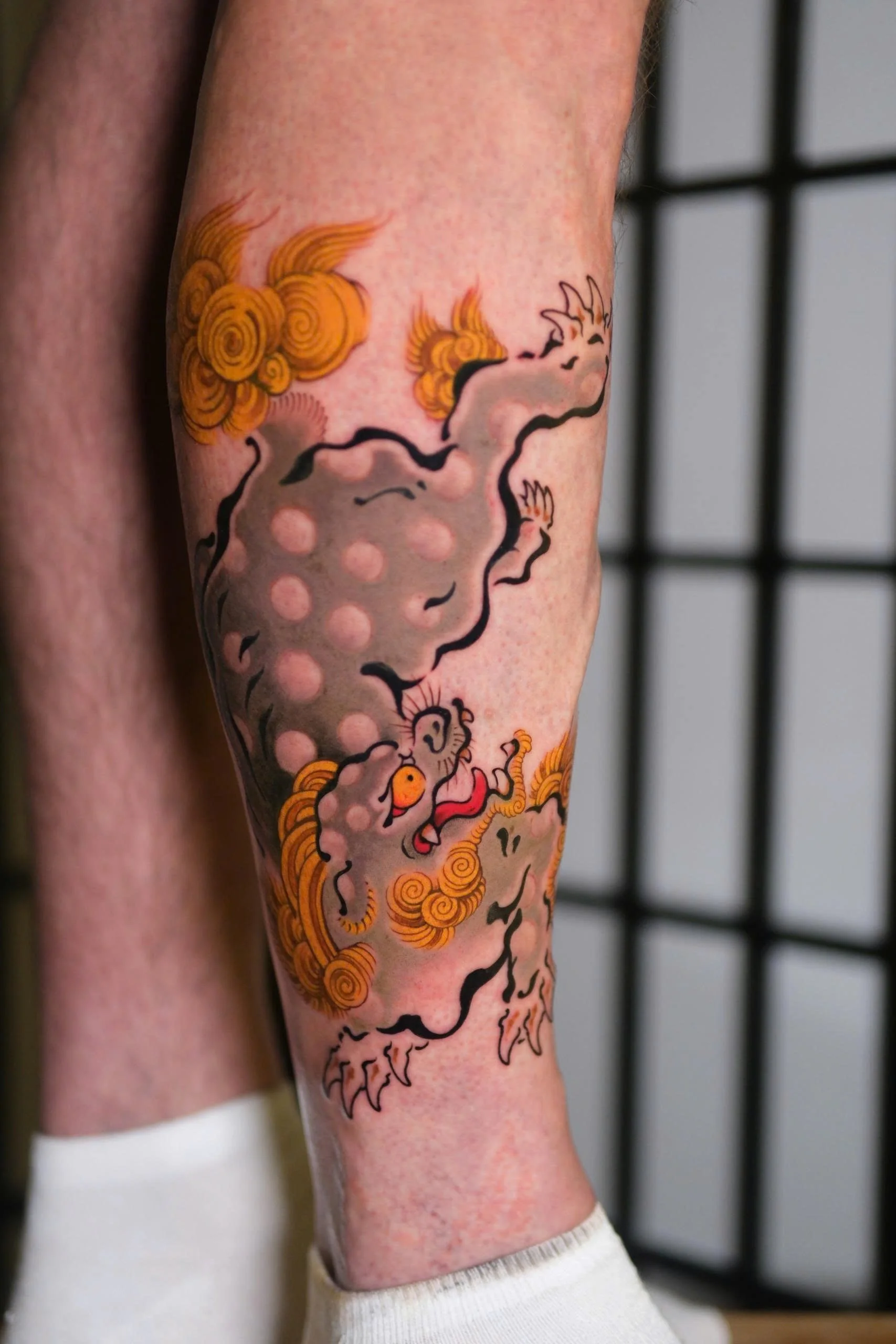 Tattoo of a mythical creature with a dragon's head and body, decorated with swirling patterns, on a person's arm.