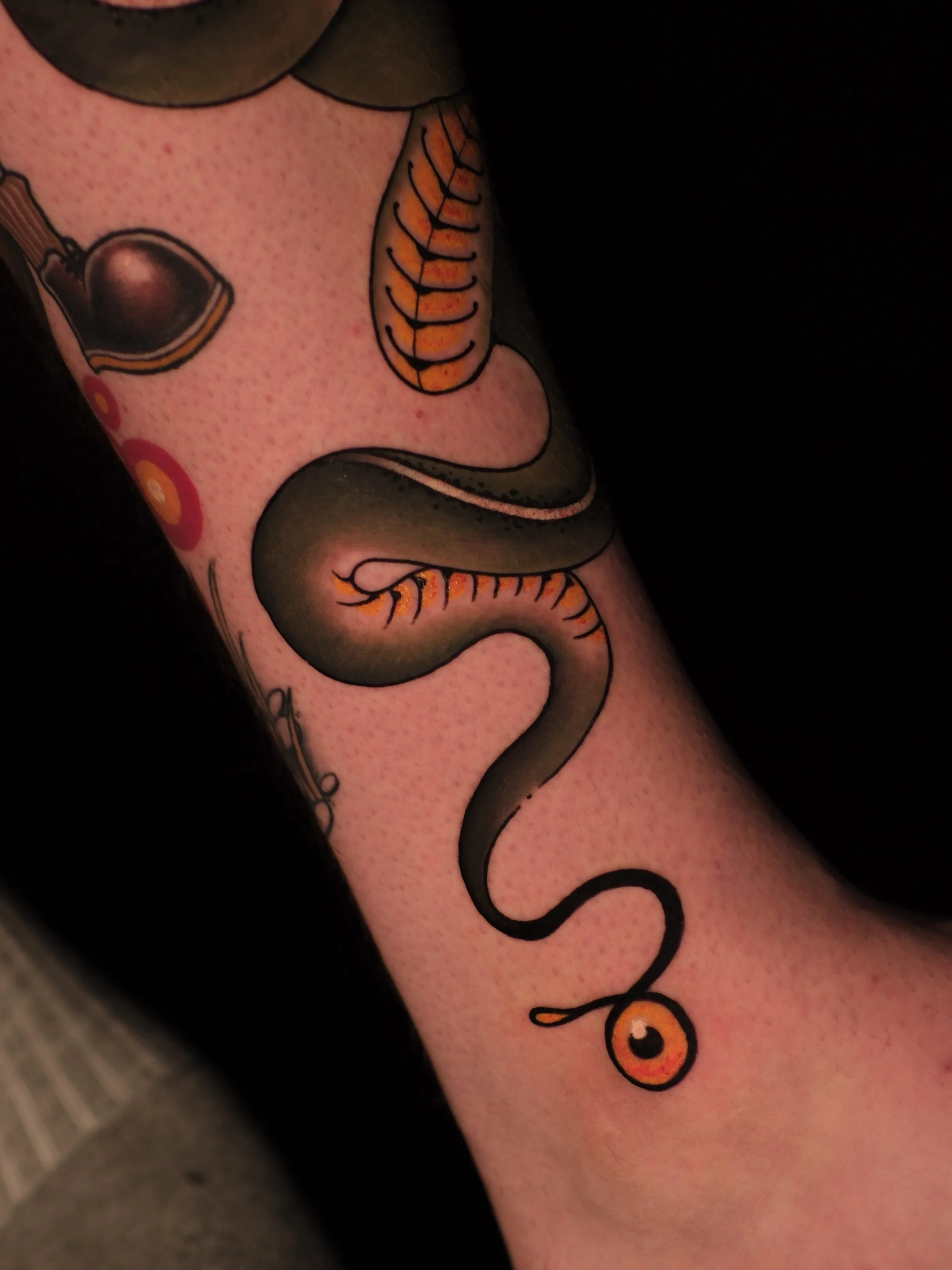 Close-up of a tattoo of a cartoonish eye, smiley face, and a curling black line on a person's arm.