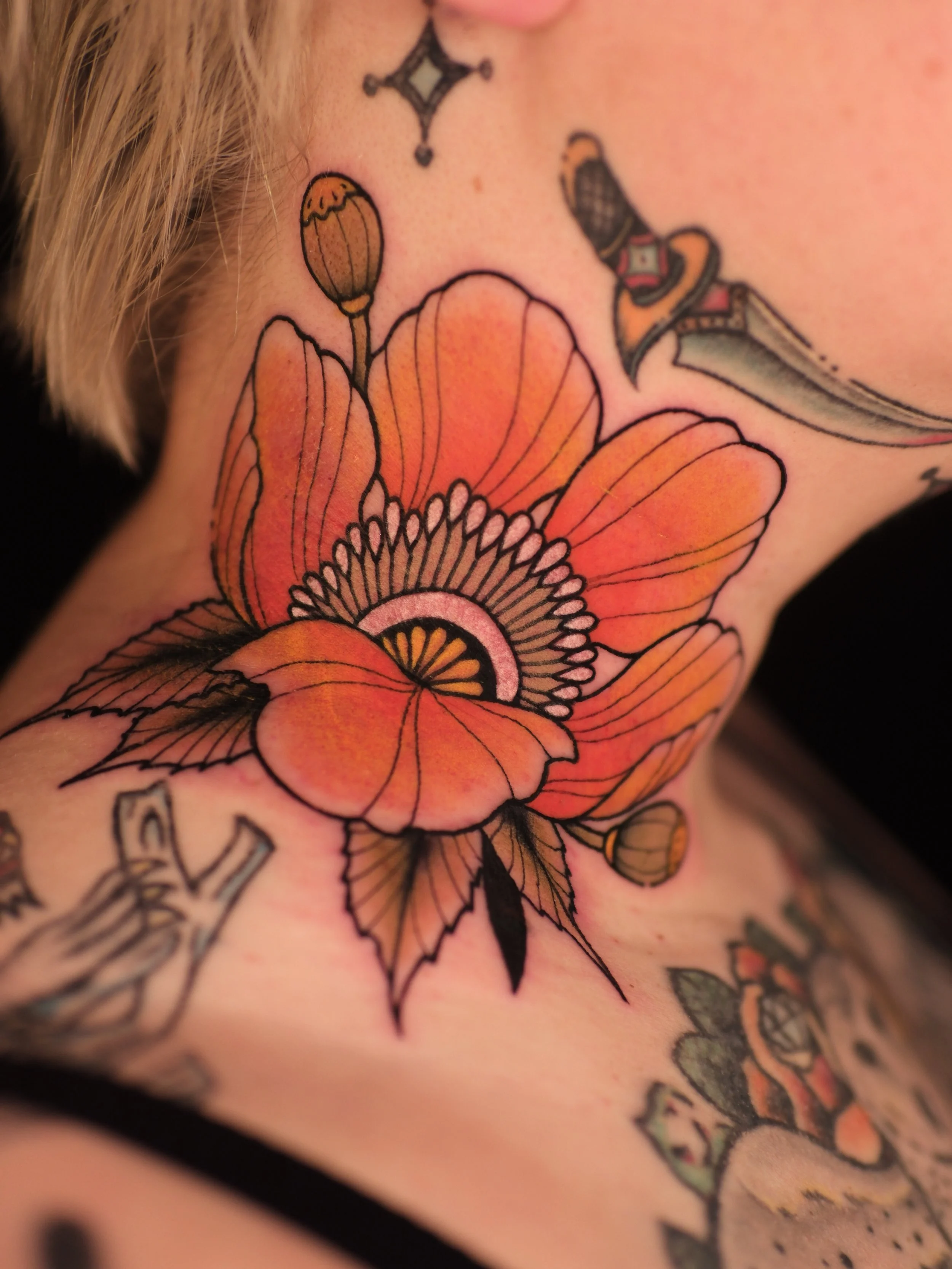 Close-up of a colorful tattoo on skin, featuring orange and pink flowers with black outlines and green leaves, and small tattoo details including a star and a snake.