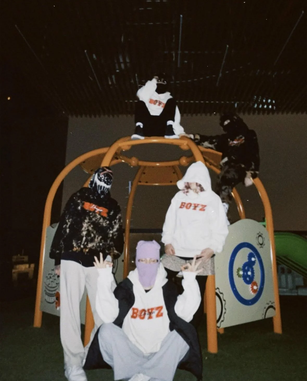 Group of people wearing Halloween costumes at night, gathered around a playground structure, some sitting and some standing.