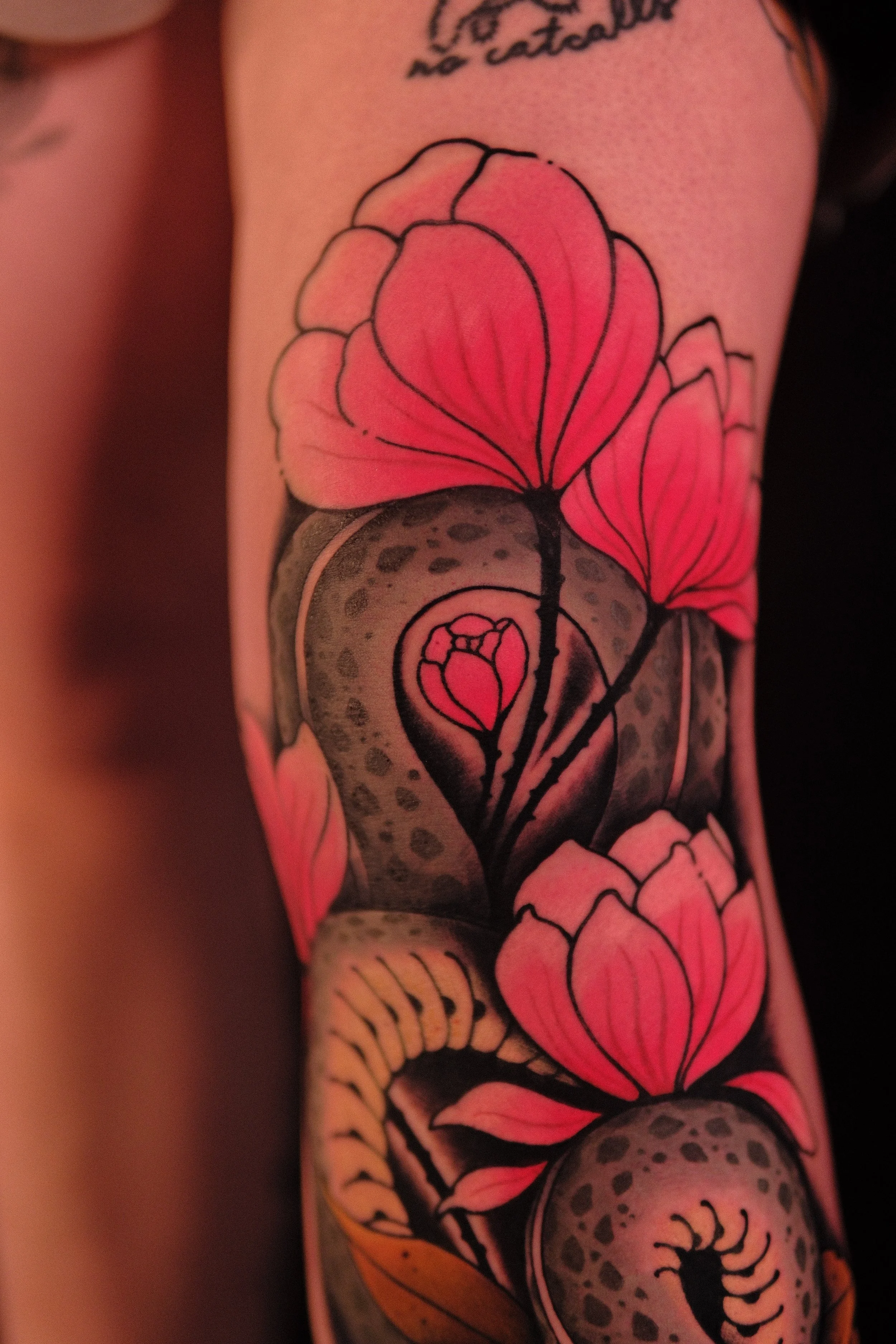 Close-up of a tattoo sleeve featuring colorful roses with black outlines, a skull with animal print, and a scorpion, all on skin, with some text partially visible.