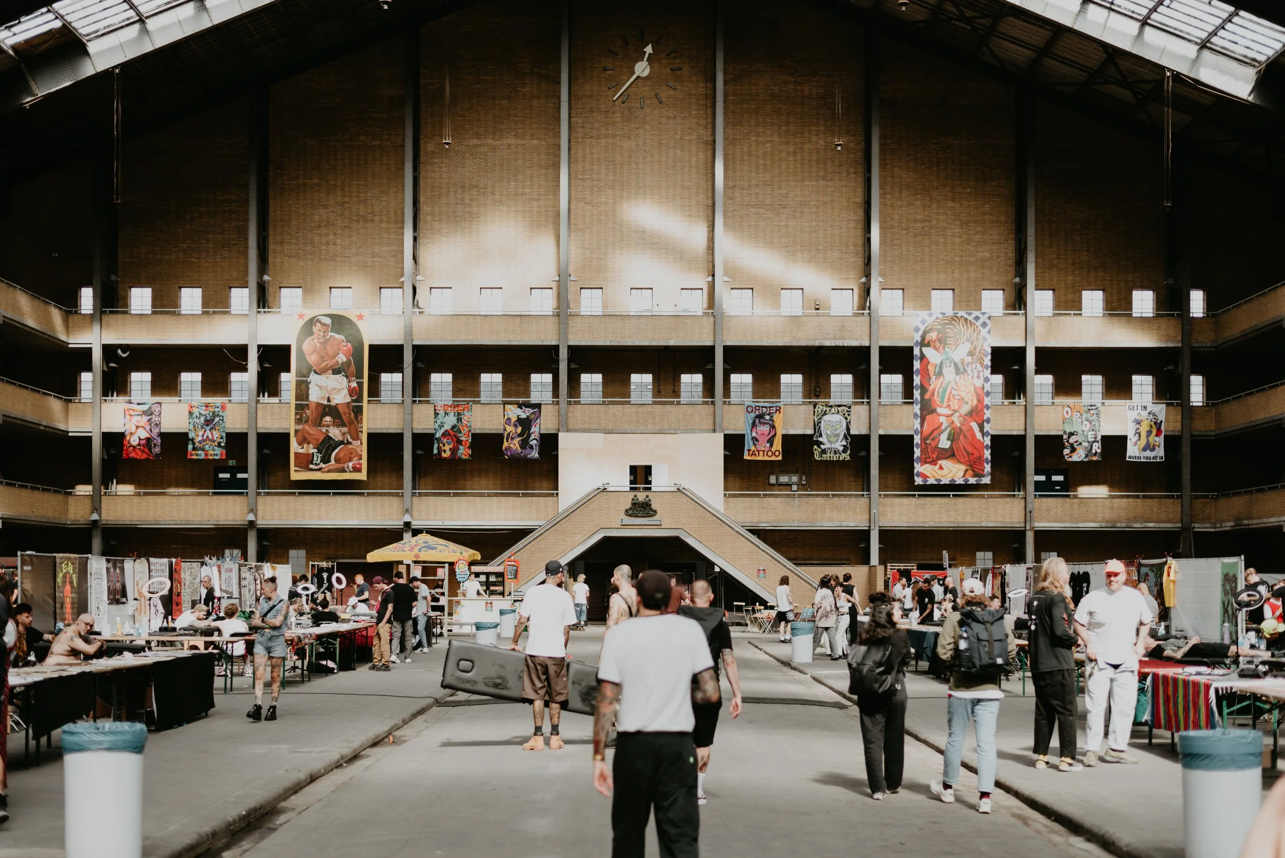 Indoor market in a large building with banners, booths, and people shopping.