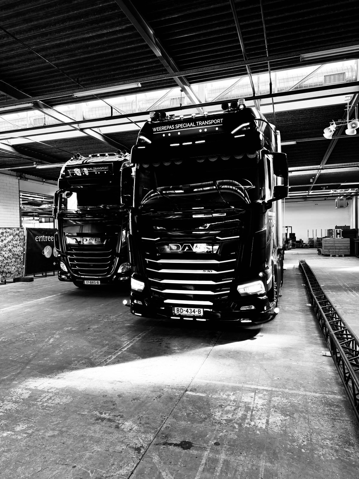Twee grote DAF-trucks in een gebouw, mogelijk een magazijn, met het bovenaan de cabine een tekst 'Weerepas speciaal transport'.